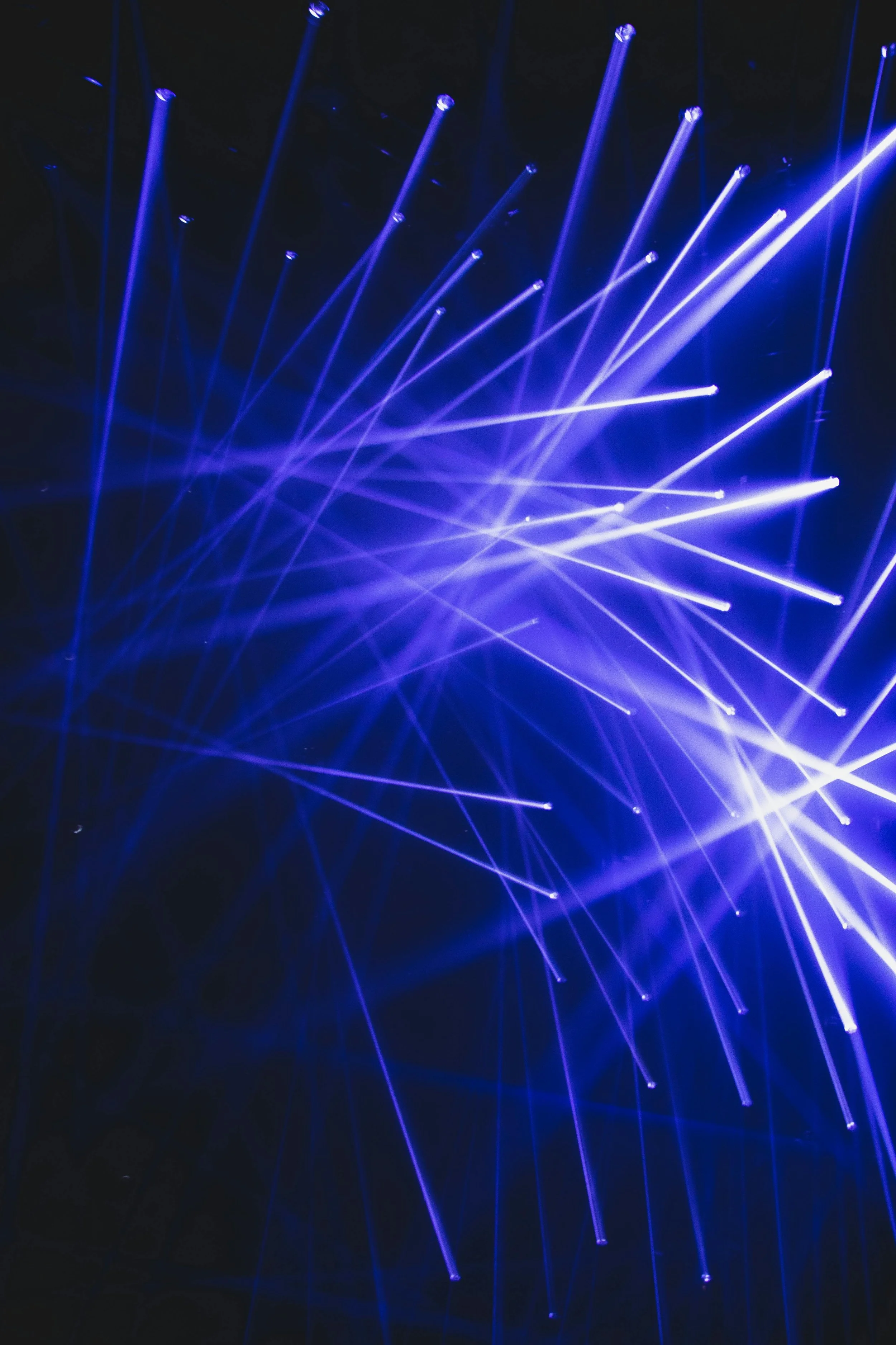Bright blue and purple laser lights crisscrossing in a dark space, creating a vibrant light display.