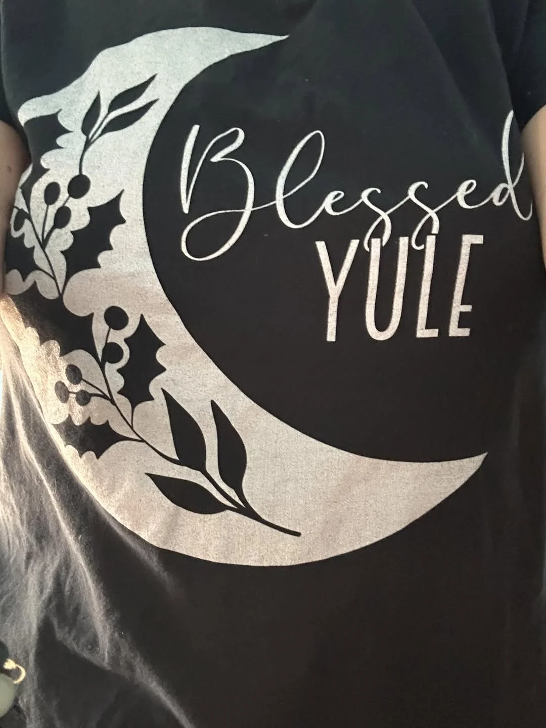 A black shirt with a crescent moon design and the words “Blessed Yule” in light lettering.