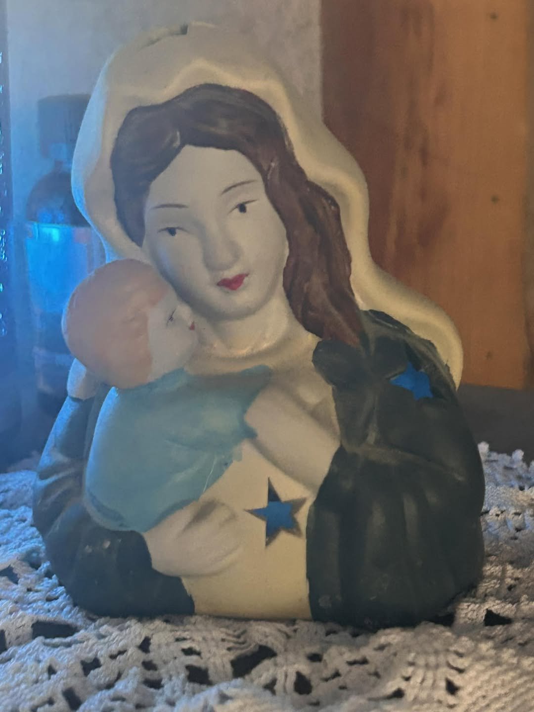 Hand-painted Madonna and child figurine resting on lace, softly lit in blue tones, symbolizing protection, gestation, and the quiet birth of new light during winter.