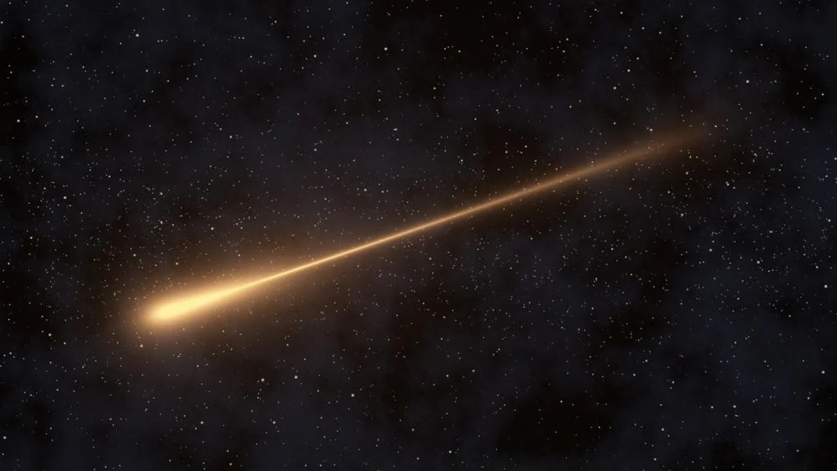A bright shooting star streaks across a dark, star-filled night sky, leaving a long glowing trail against the blackness.