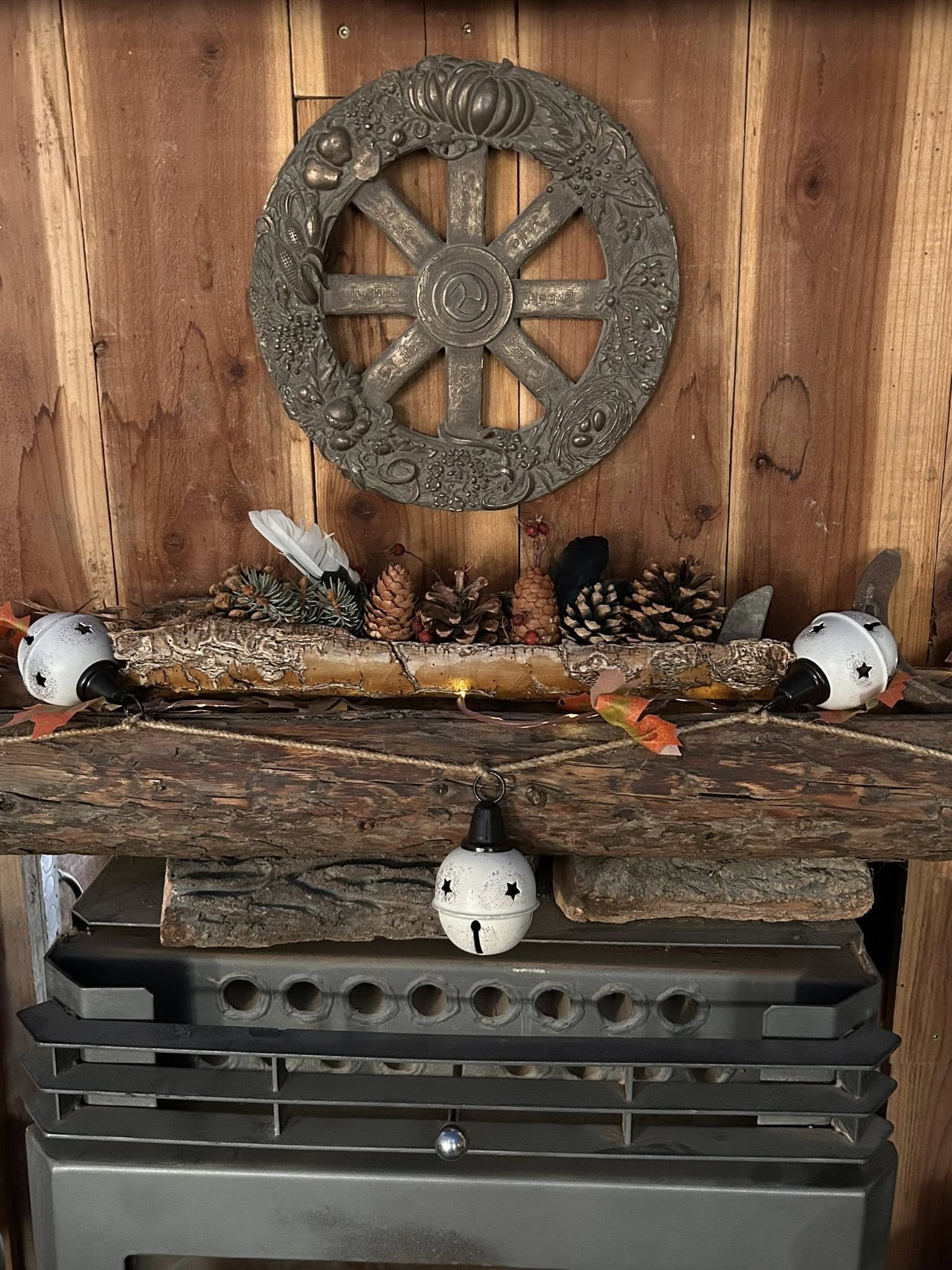A handmade Yule log arranged with bark, pinecones, feathers, and natural elements resting on a wooden hearth beneath a seasonal wheel.