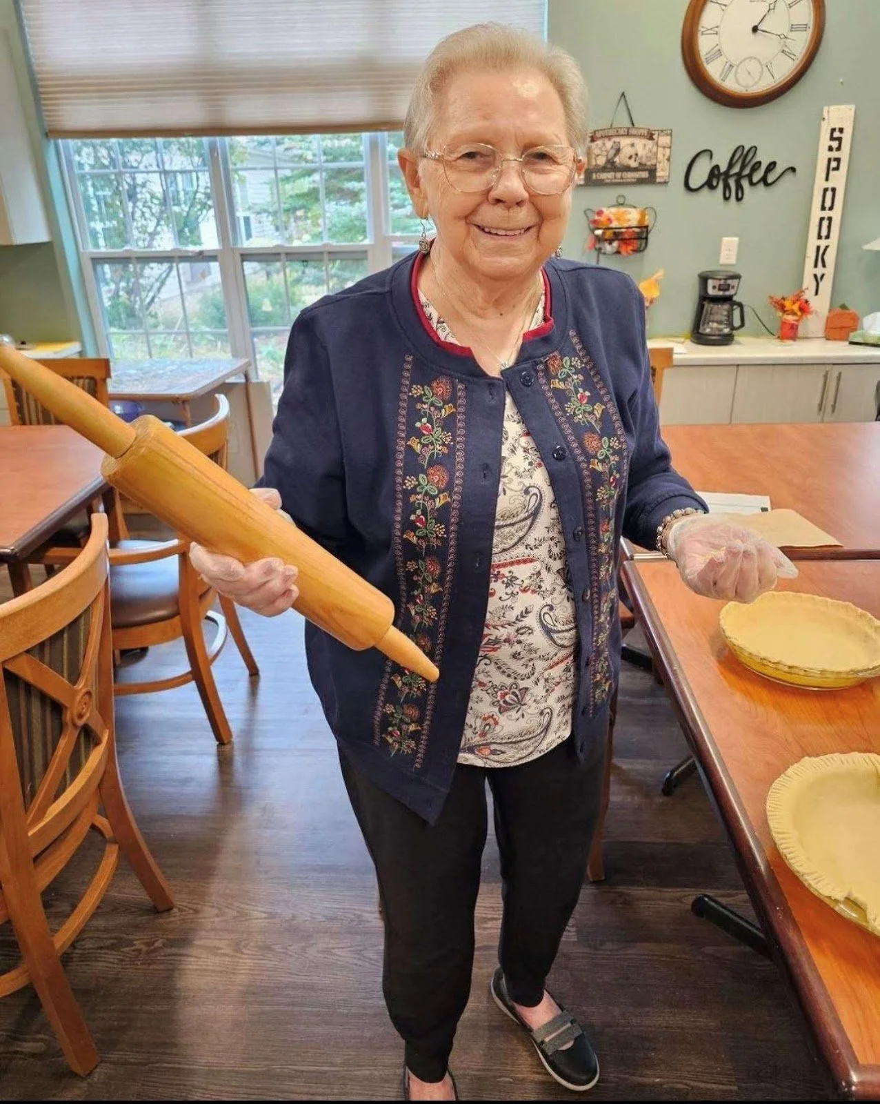Elderly woman smiling while preparing pies in assisted living community kitchen.