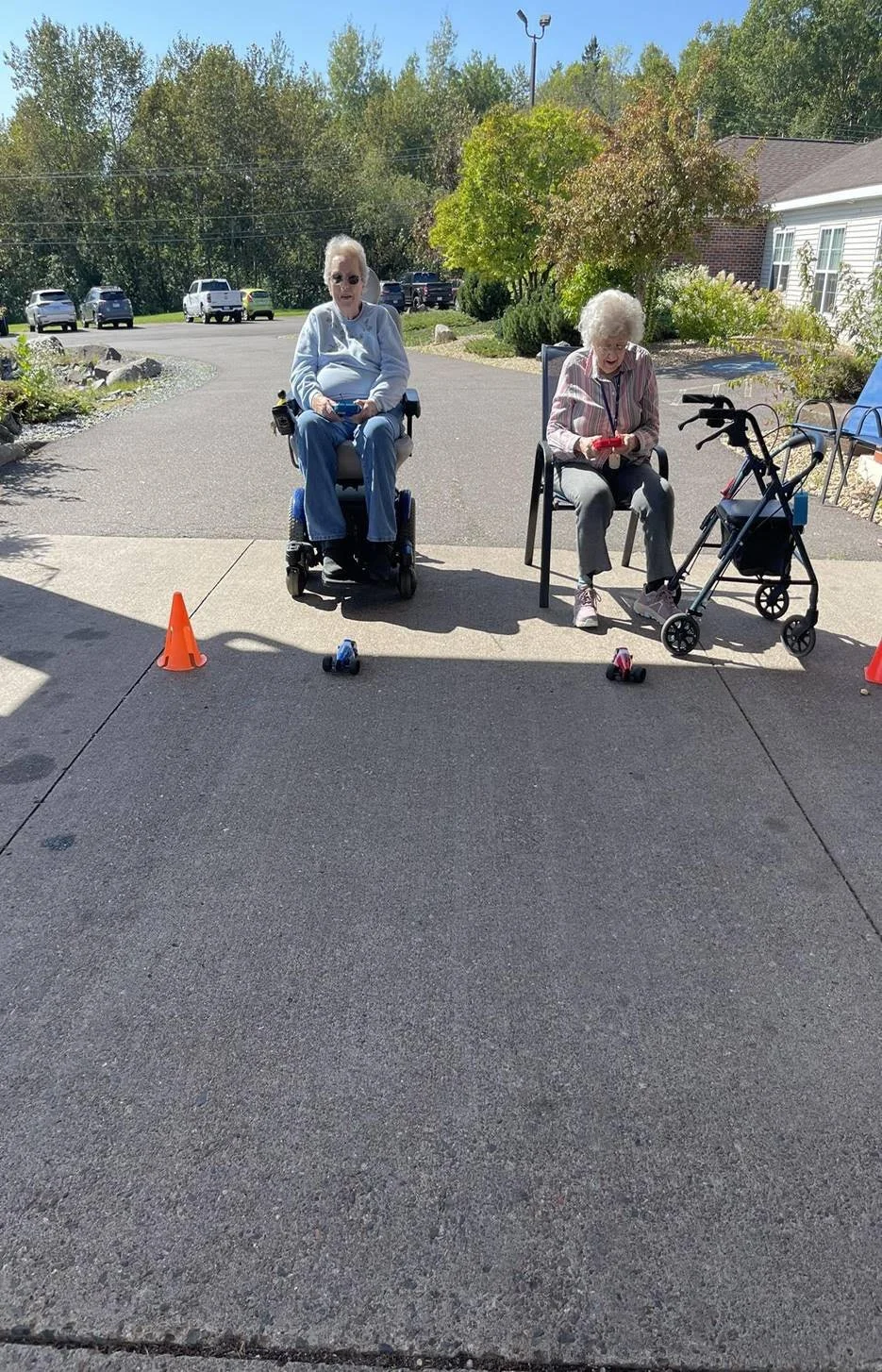 One senior is sitting on the motor wheelchair and another on a chair in an assisted living facility.