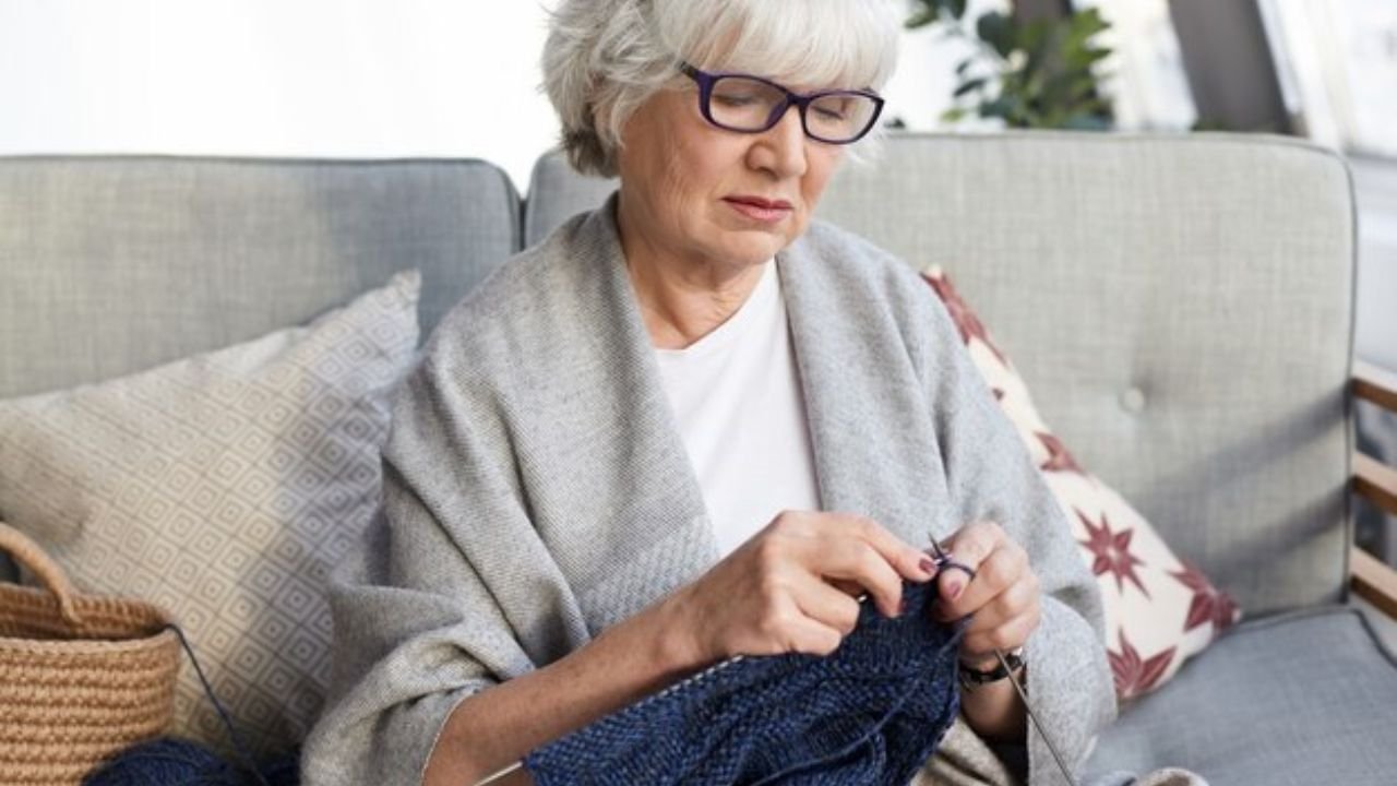 Senior knitting with yarn in a cozy assisted living setting.