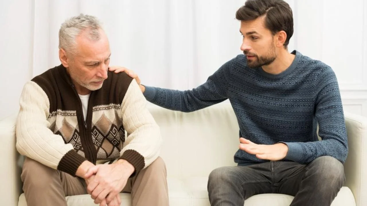 Young guy with hand on shoulder of aged sad man on sofa