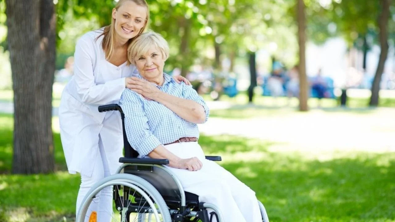 Caregiver supporting wheelchair user outdoors in assisted living.