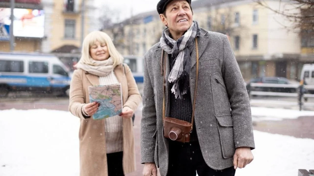 Seniors exploring snowy city with camera and map.