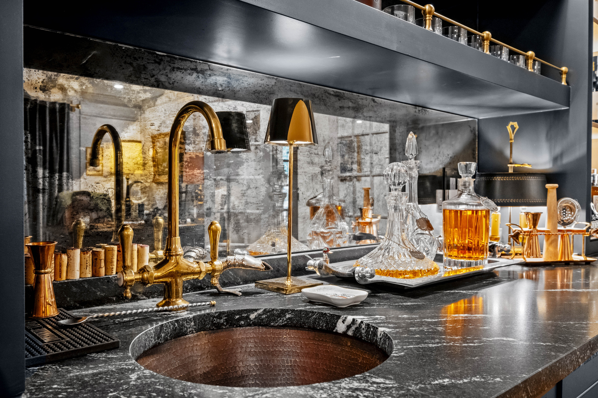 Luxurious bar area with black marble countertop, gold fixtures, glass decanters filled with amber liquor, and a reflective mirror behind the counter.