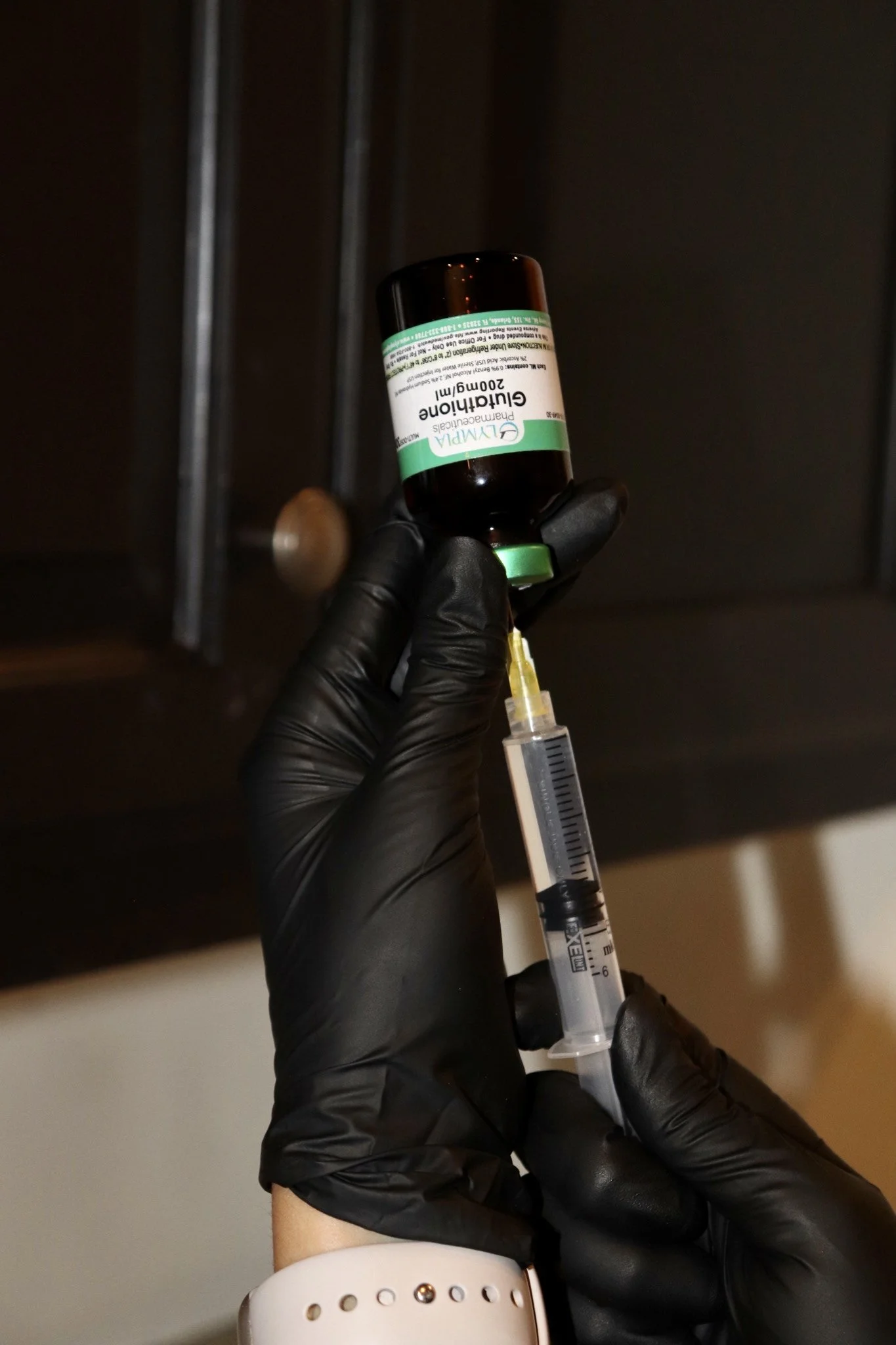 A person wearing a black glove holding a syringe and a bottle of medication in a dimly lit room.
