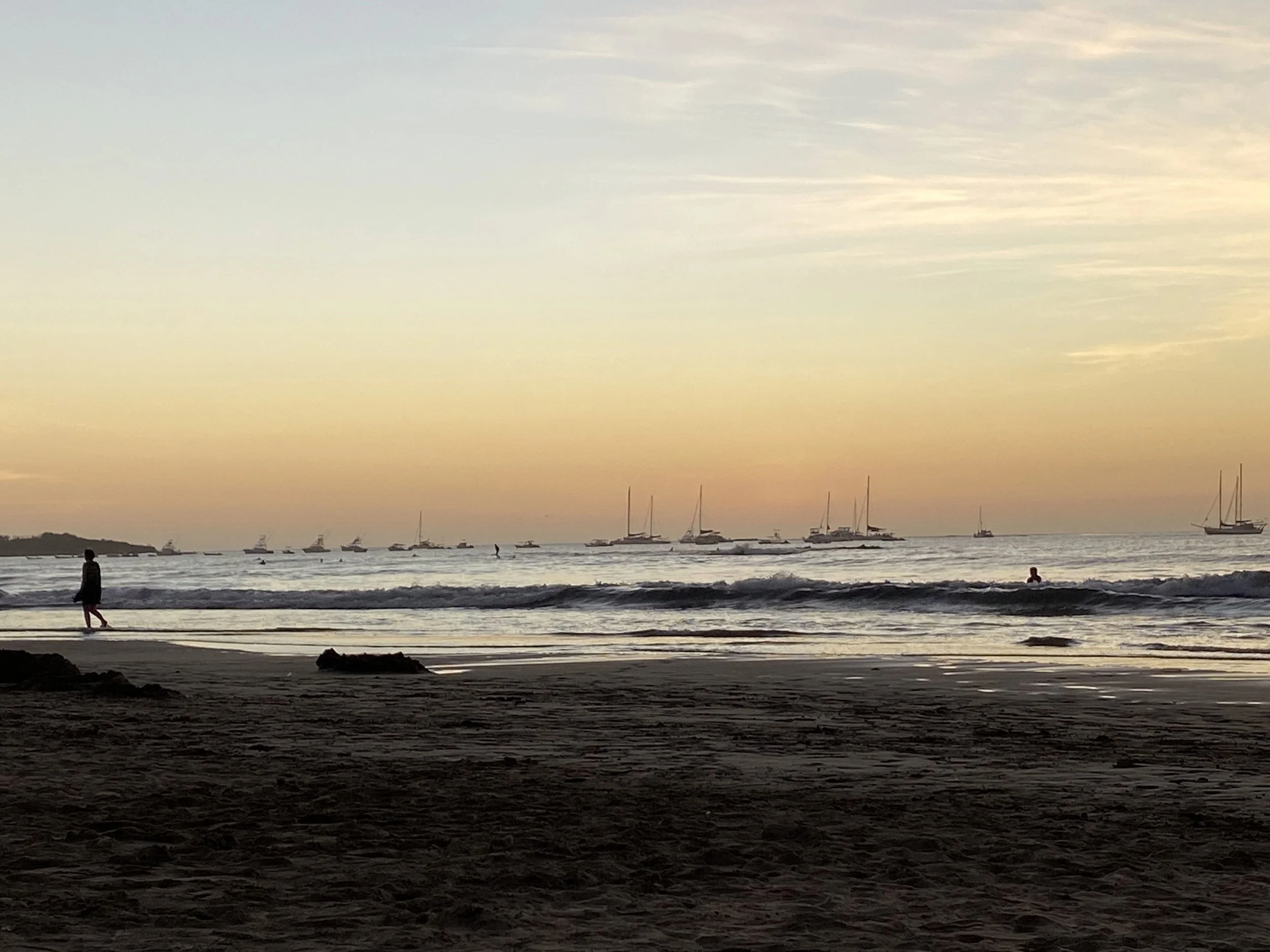 Catamarans anchored offshore at sunset near Tamarindo Beach in Costa Rica, with gentle waves, a sandy beach, and a golden sky over the Pacific Ocean.