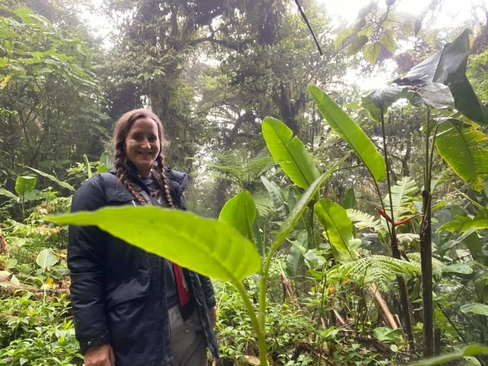A traveller wearing a dark jacket stands smiling among lush green plants in Monteverde's cloud forest in Costa Rica.
