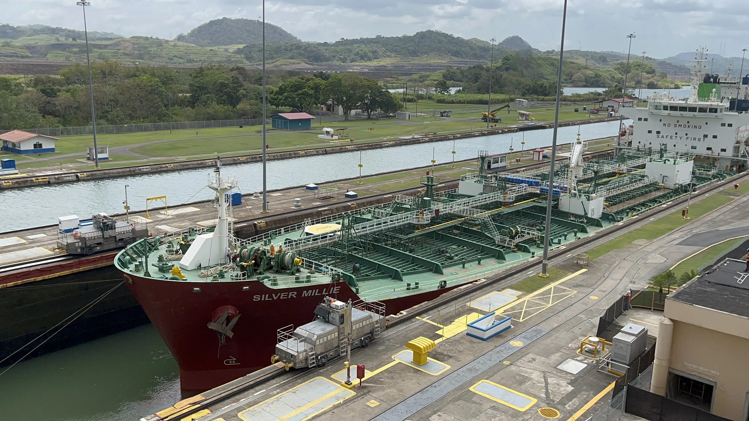 Large cargo ship passing through the Miraflores Locks of the Panama Canal, surrounded by lock machinery and green hills.