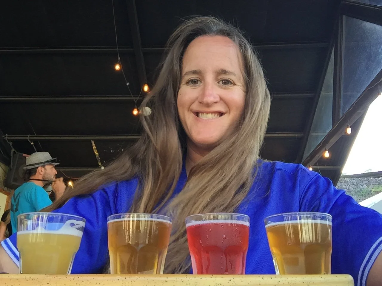 A smiling woman in a blue shirt sitting behind a tasting flight of four drinks at Boquete Brewing Company in Panama.