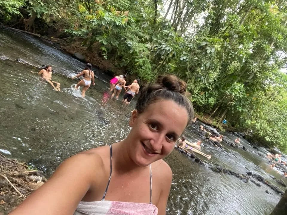 Natural hot springs near Arenal Volcano in La Fortuna, Costa Rica, with people relaxing in the warm river surrounded by rainforest.