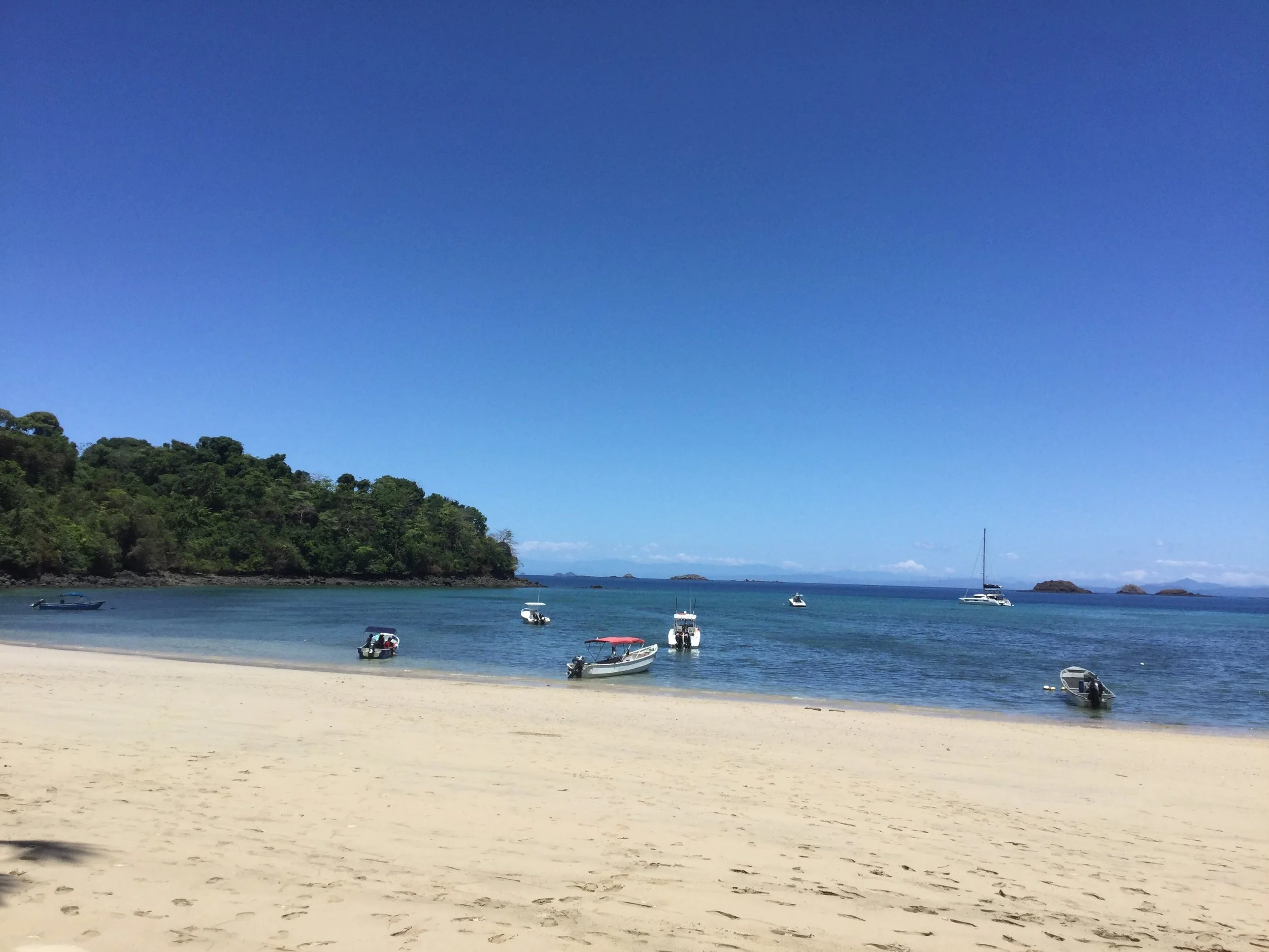 Small motorboats anchored in calm blue water off the sandy shore of Playa Santa Catalina, Panama.