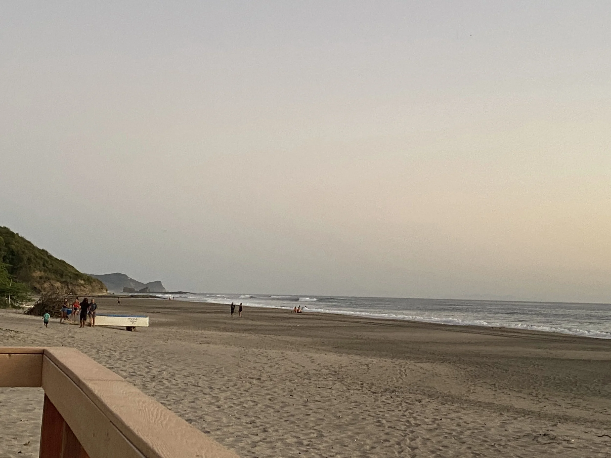 View of Popoyo Beach in Nicaragua with a wide sandy shoreline, gentle Pacific waves, and a few people walking along the beach on a peaceful afternoon.