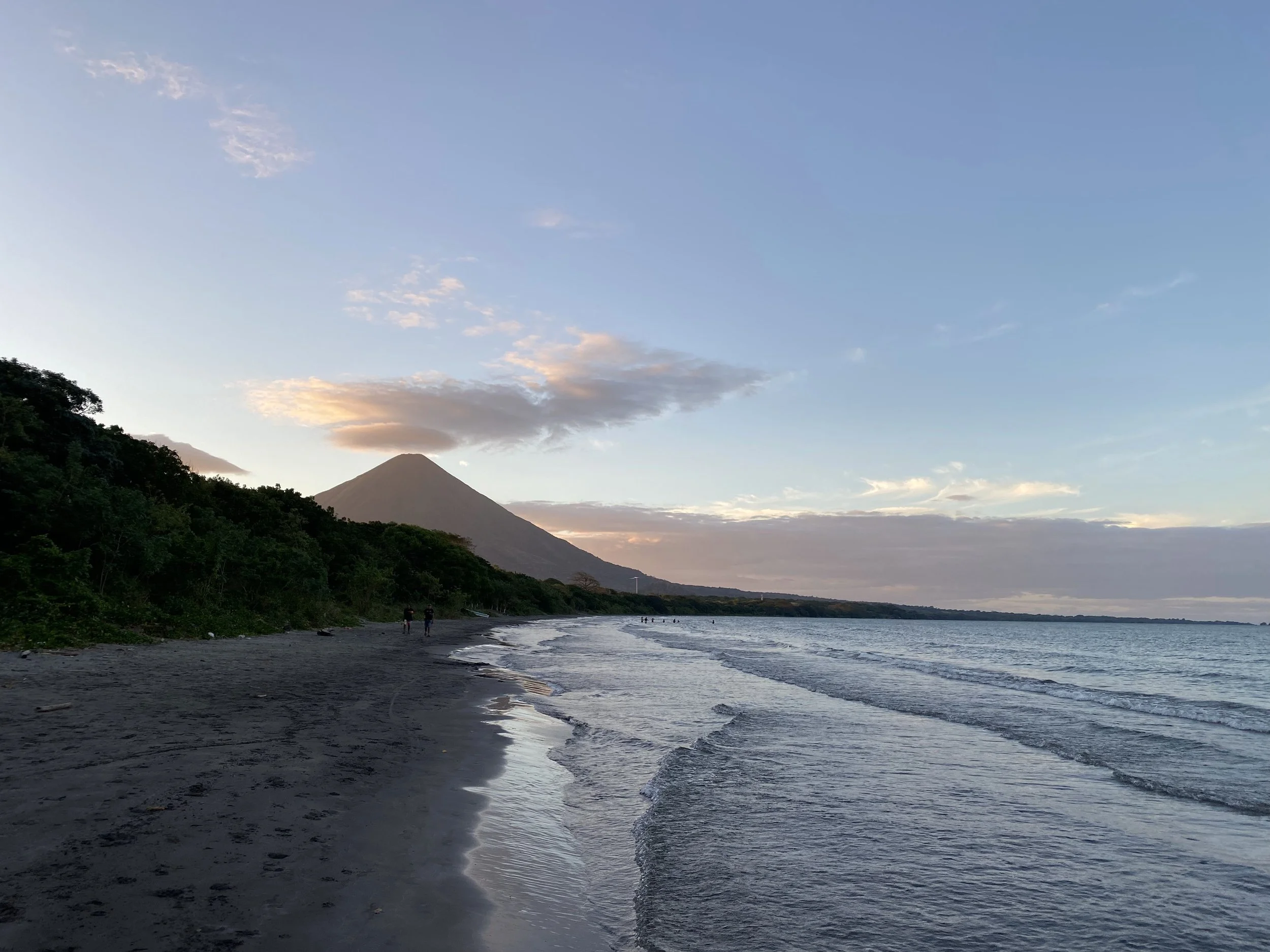 Sunset view of a beach on Ometepe Island in Nicaragua with gentle waves and a volcano rising in the background.