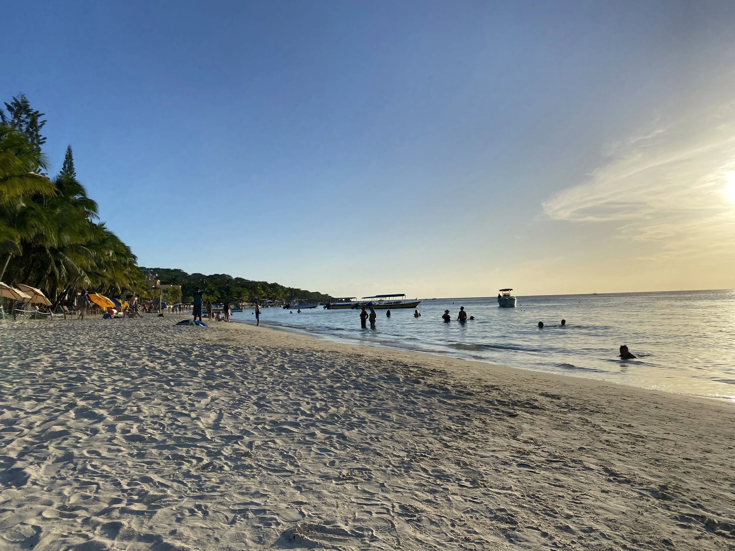 West Bay Beach in Roatán, Honduras with white sand, calm Caribbean water, and people swimming at sunset