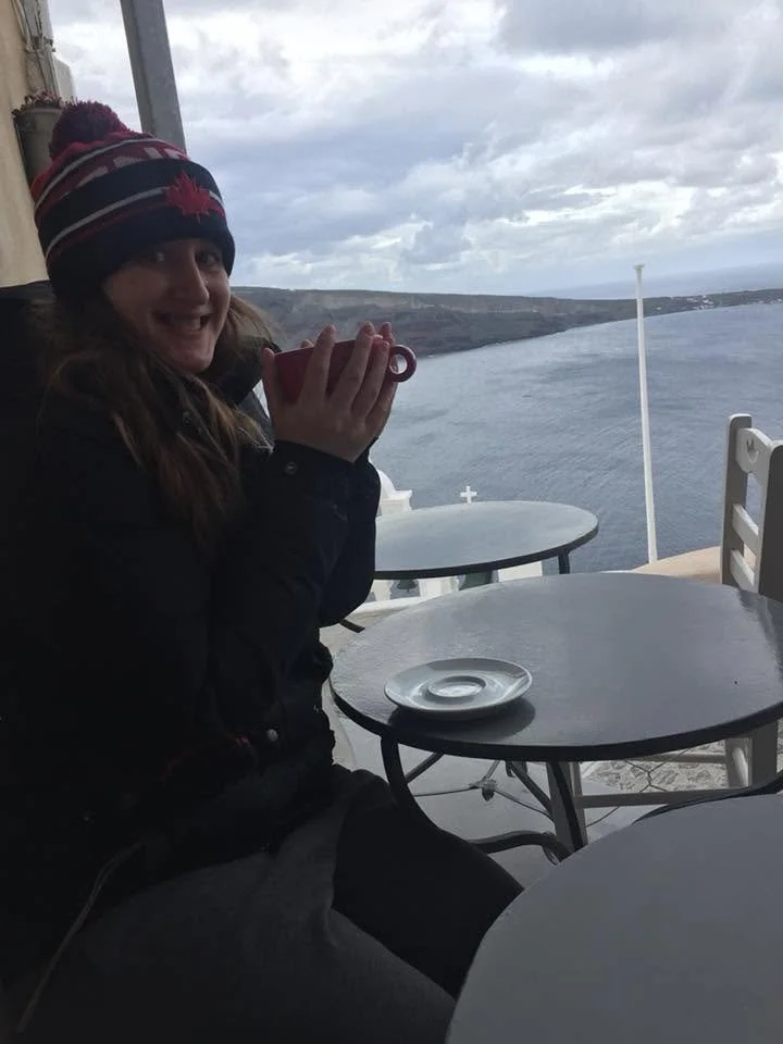Solo female traveler enjoying a hot drink with a view over Santorini, Greece after a delayed ferry created extra time to relax and enjoy the island.