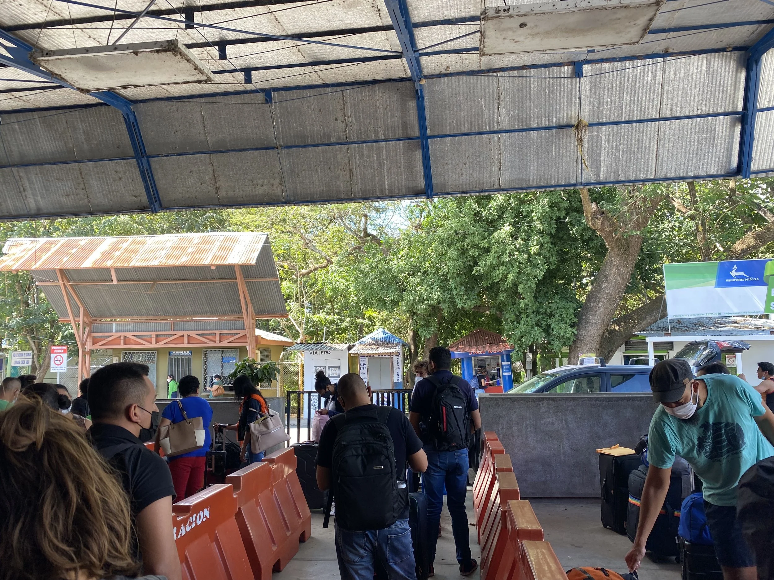 Travellers with backpacks waiting in a long immigration queue at the Nicaragua–Costa Rica border crossing, with ticket booths visible in the background.