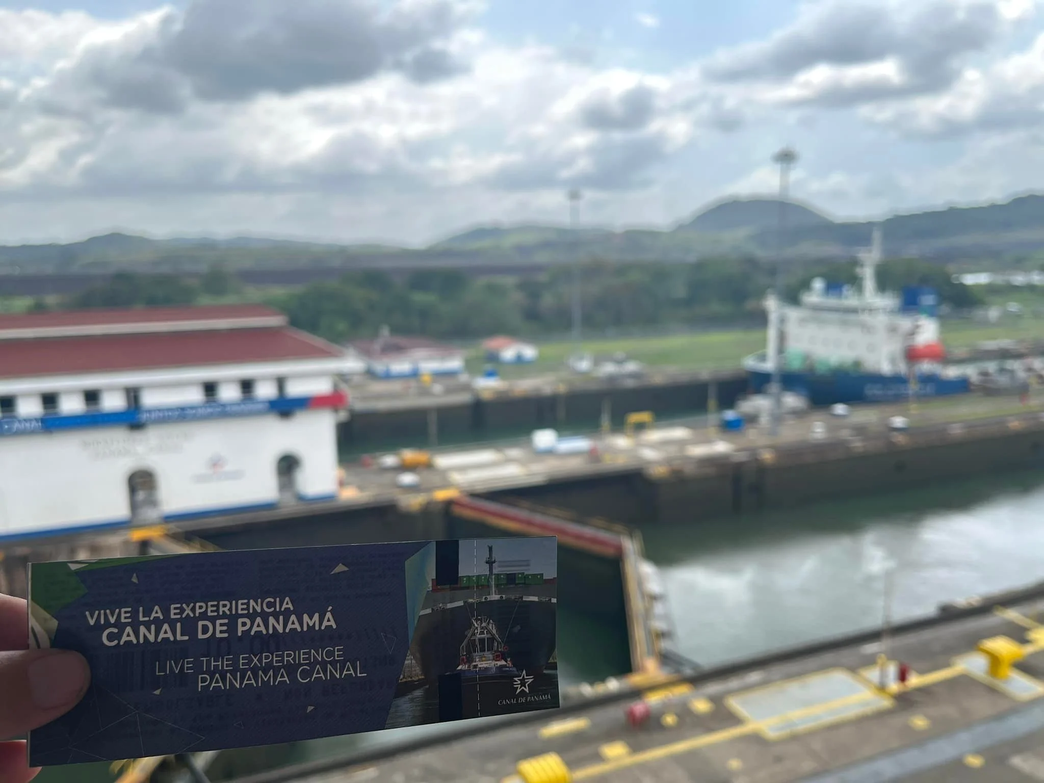 Panama Canal admission ticket held in front of the Miraflores Locks with a ship passing through the canal.