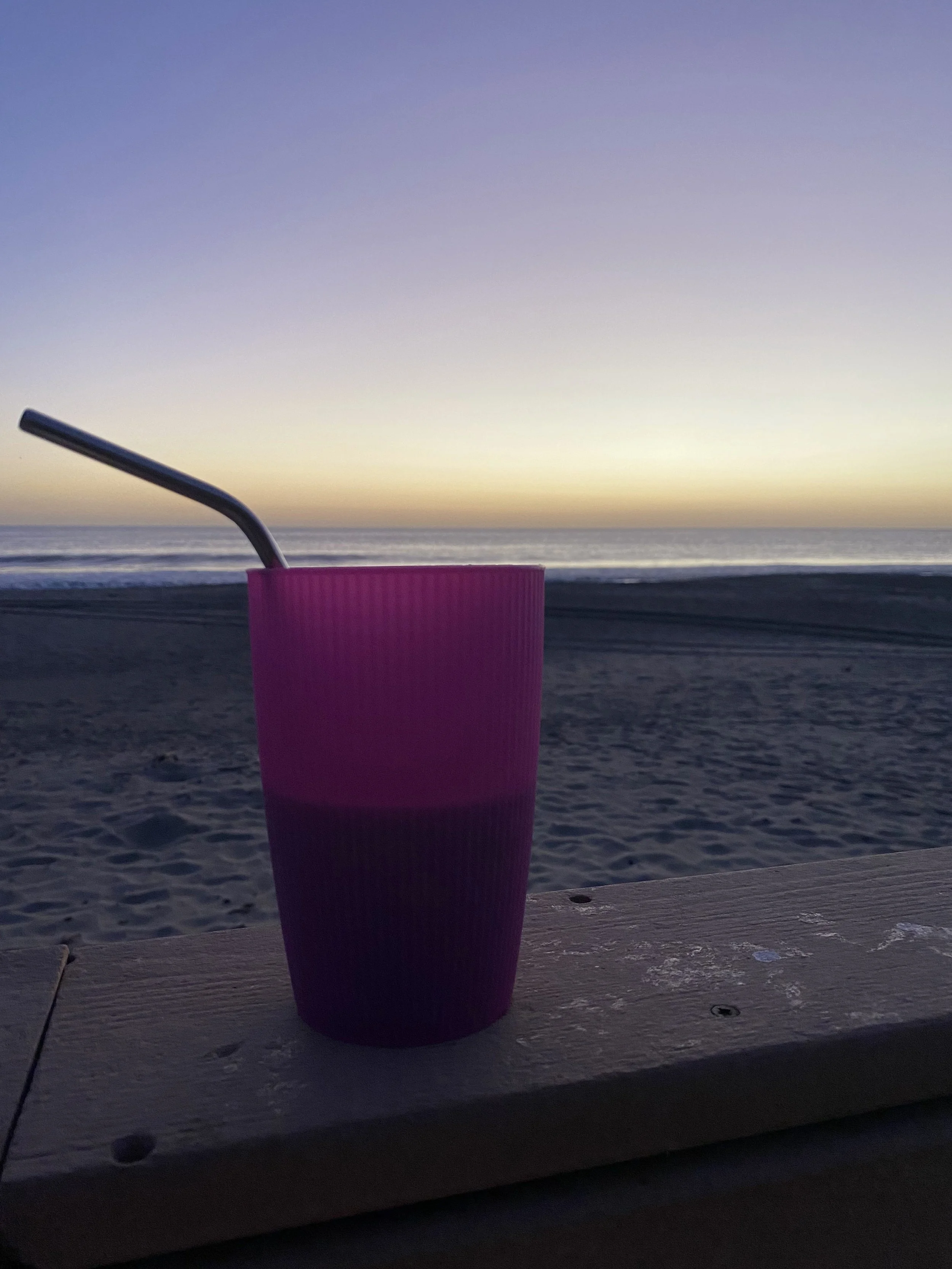 A pink cup holding a rum and coke sits on a railing overlooking the beach at sunset in Popoyo, Nicaragua.