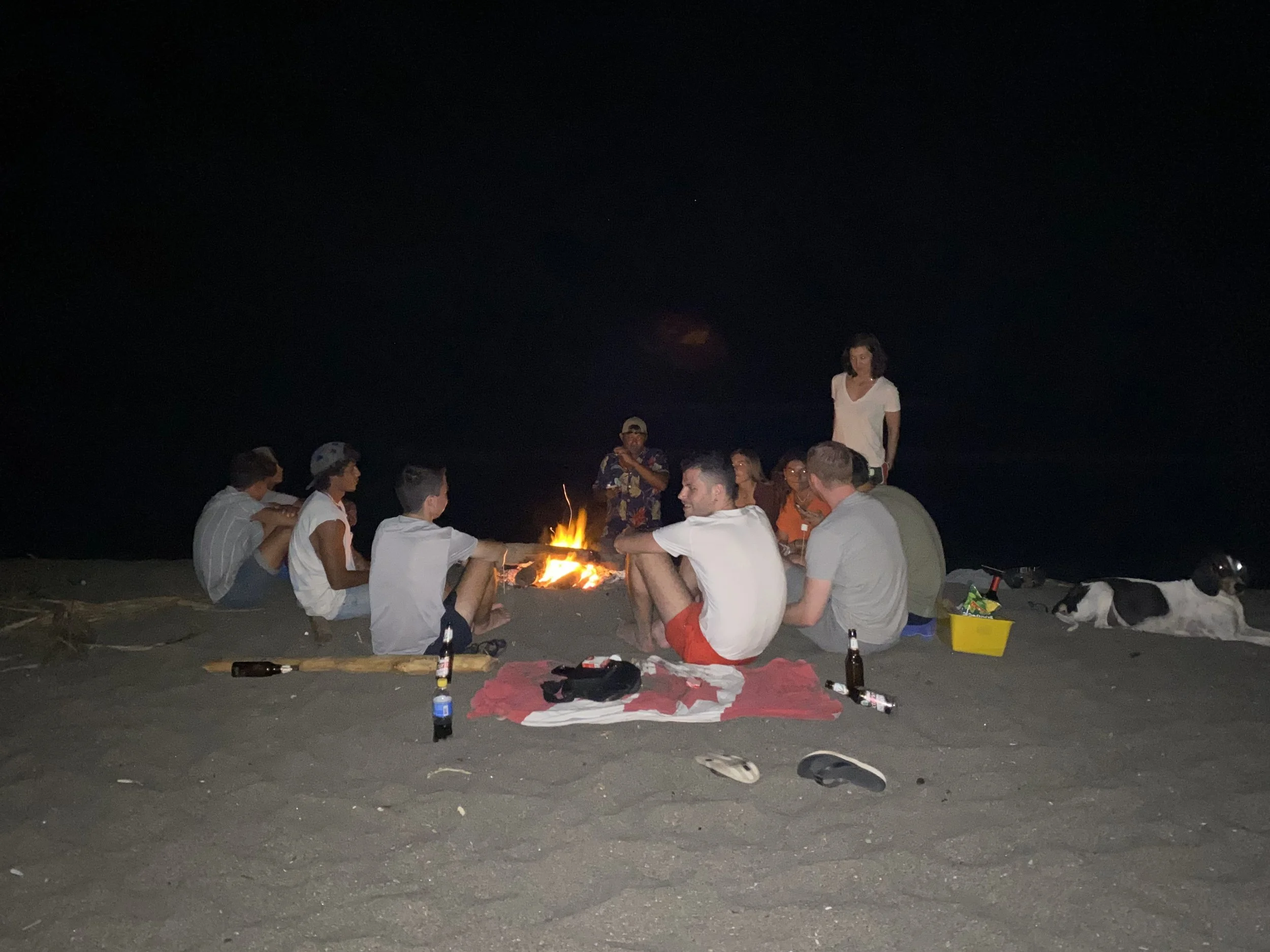 Group of travelers sitting around a bonfire on a beach at night in Las Peñitas, Nicaragua