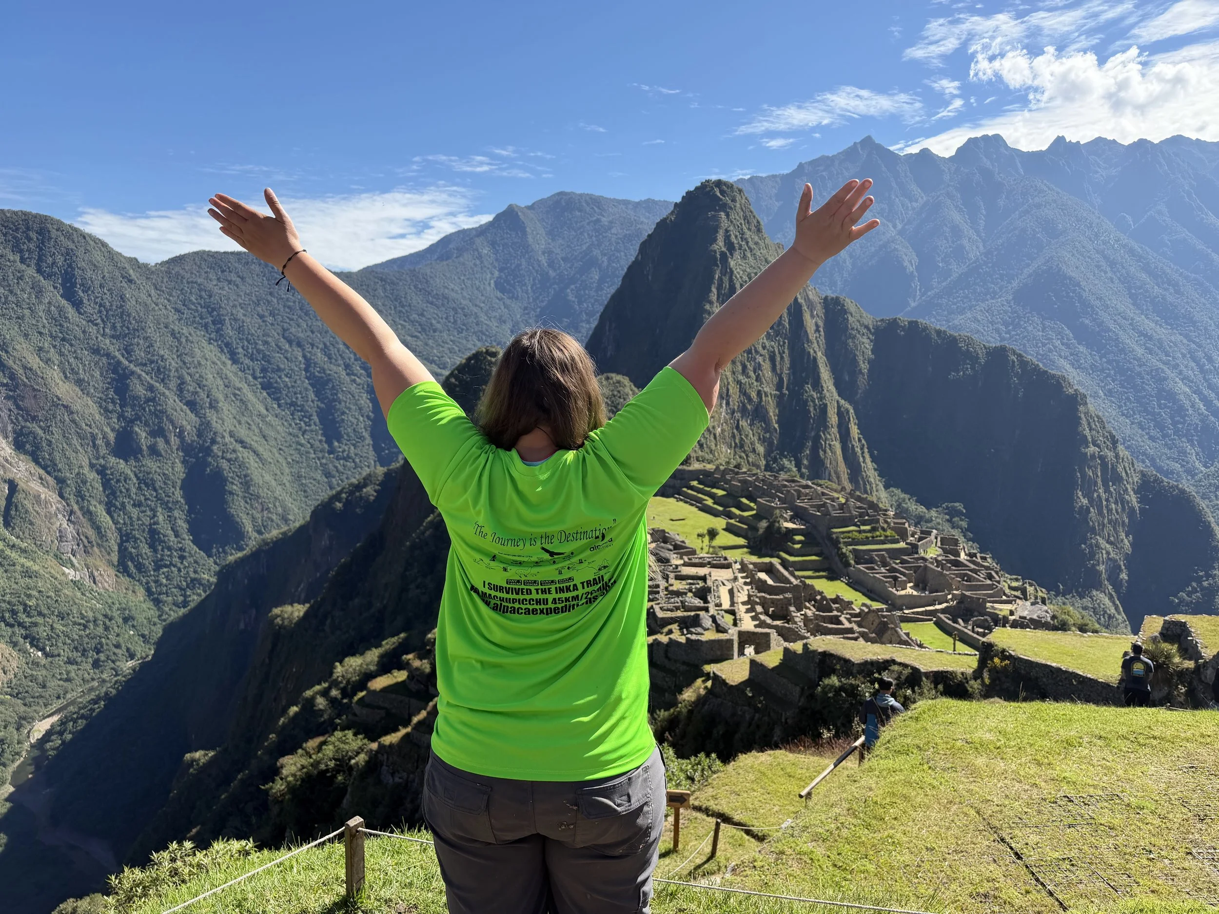 Solo female traveler wearing an 'I Survived the Inca Trail' shirt overlooking Machu Picchu in Peru after completing the four-day hike.