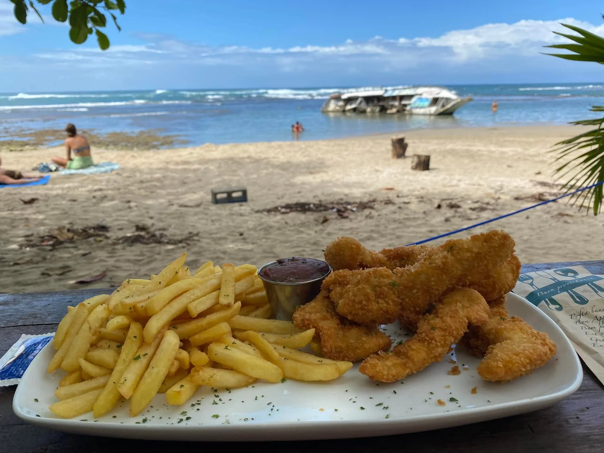 Plate of chicken tenders and French fries served at a beachfront restaurant in Puerto Viejo, Costa Rica, with the sandy beach and Caribbean Sea in the background.