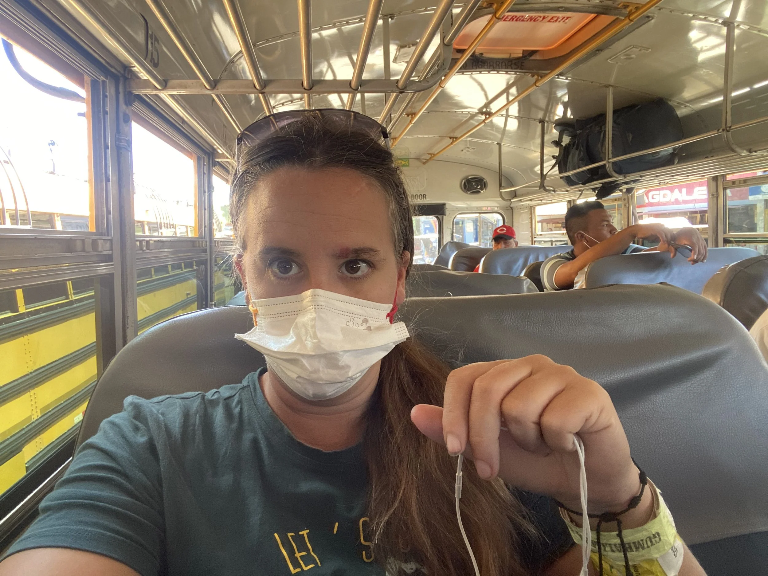 Solo female traveler wearing a mask sitting inside a local chicken bus in Nicaragua with other passengers