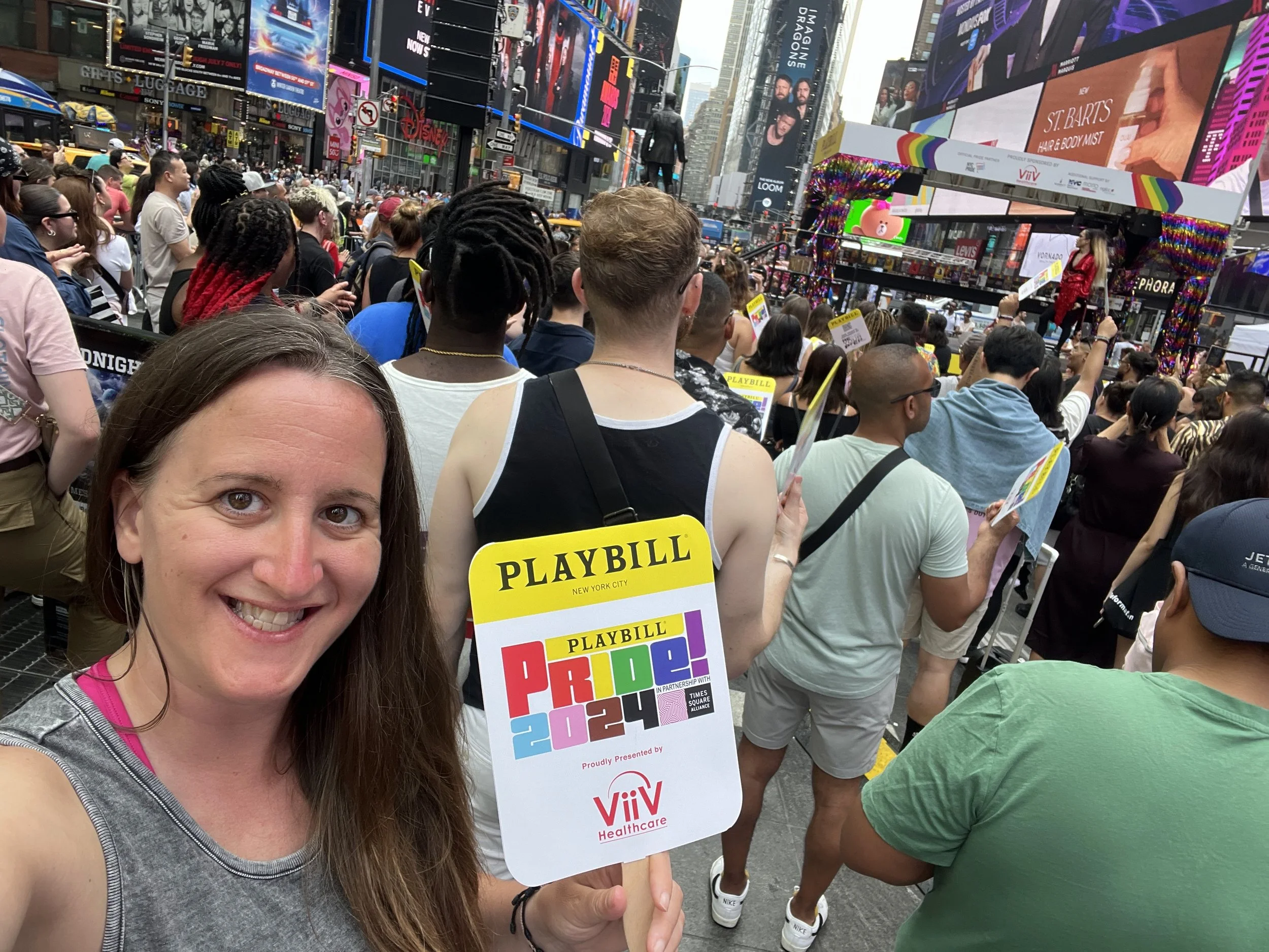 A woman holding a Pride 2024 fan in Times Square during a drag performance.