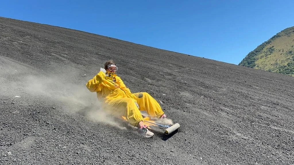 Solo traveler volcano boarding down Cerro Negro in Nicaragua wearing a yellow jumpsuit and goggles