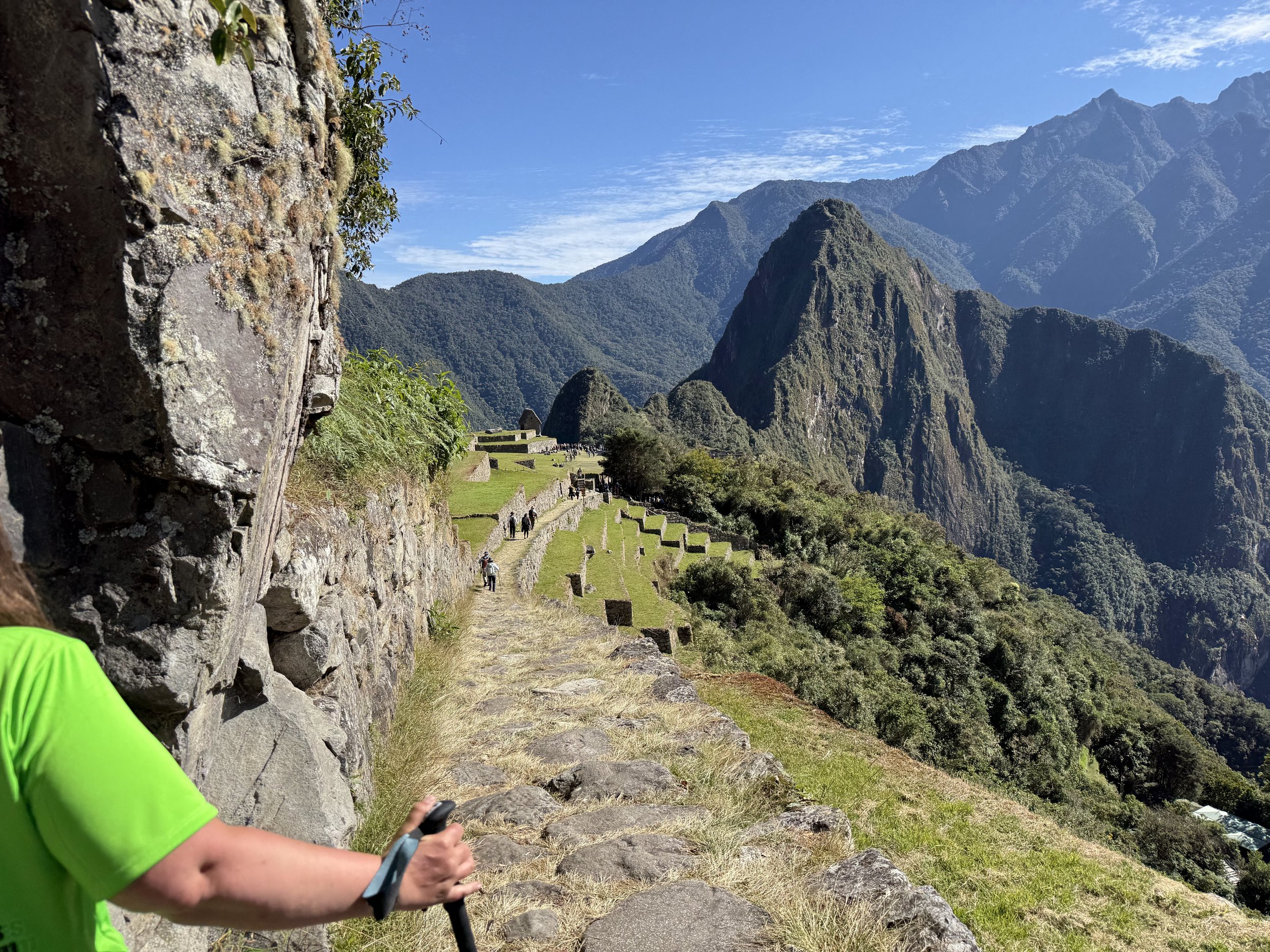 A traveller walking along the stone pathways of Machu Picchu, Peru, overlooking the ancient Inca ruins and surrounding Andes Mountains on a sunny day.