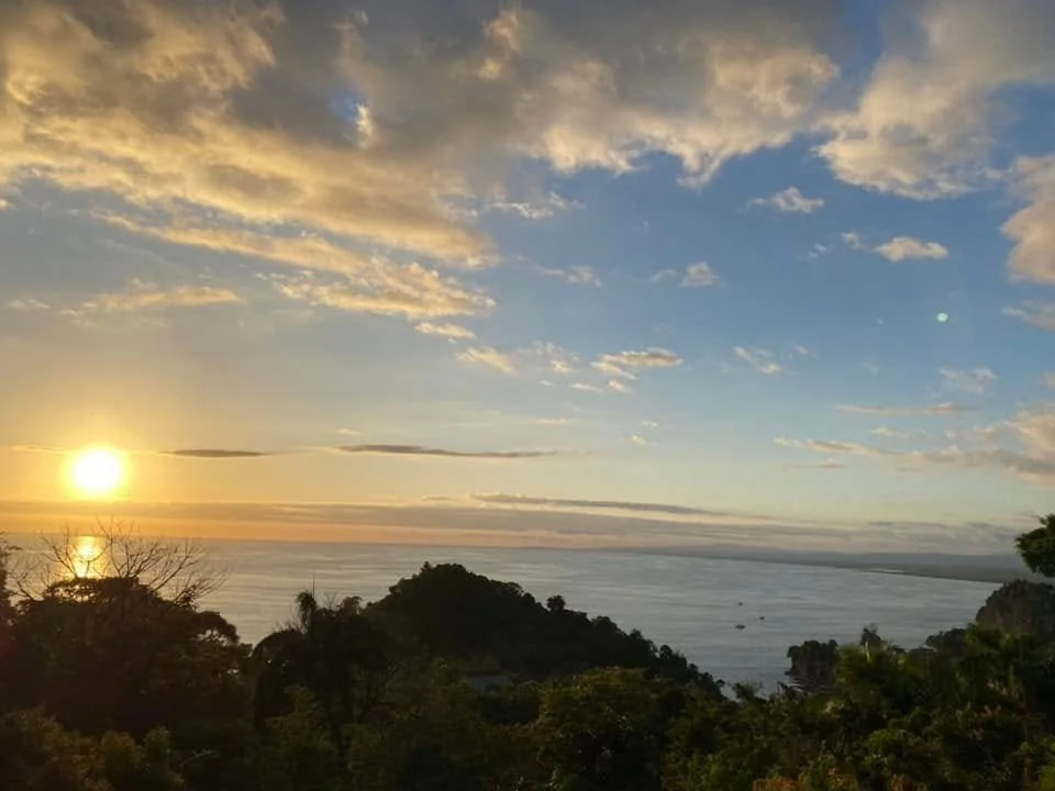 Golden sunset over the Pacific Ocean and forested coastline viewed from a roadside overlook in Manuel Antonio, Costa Rica.