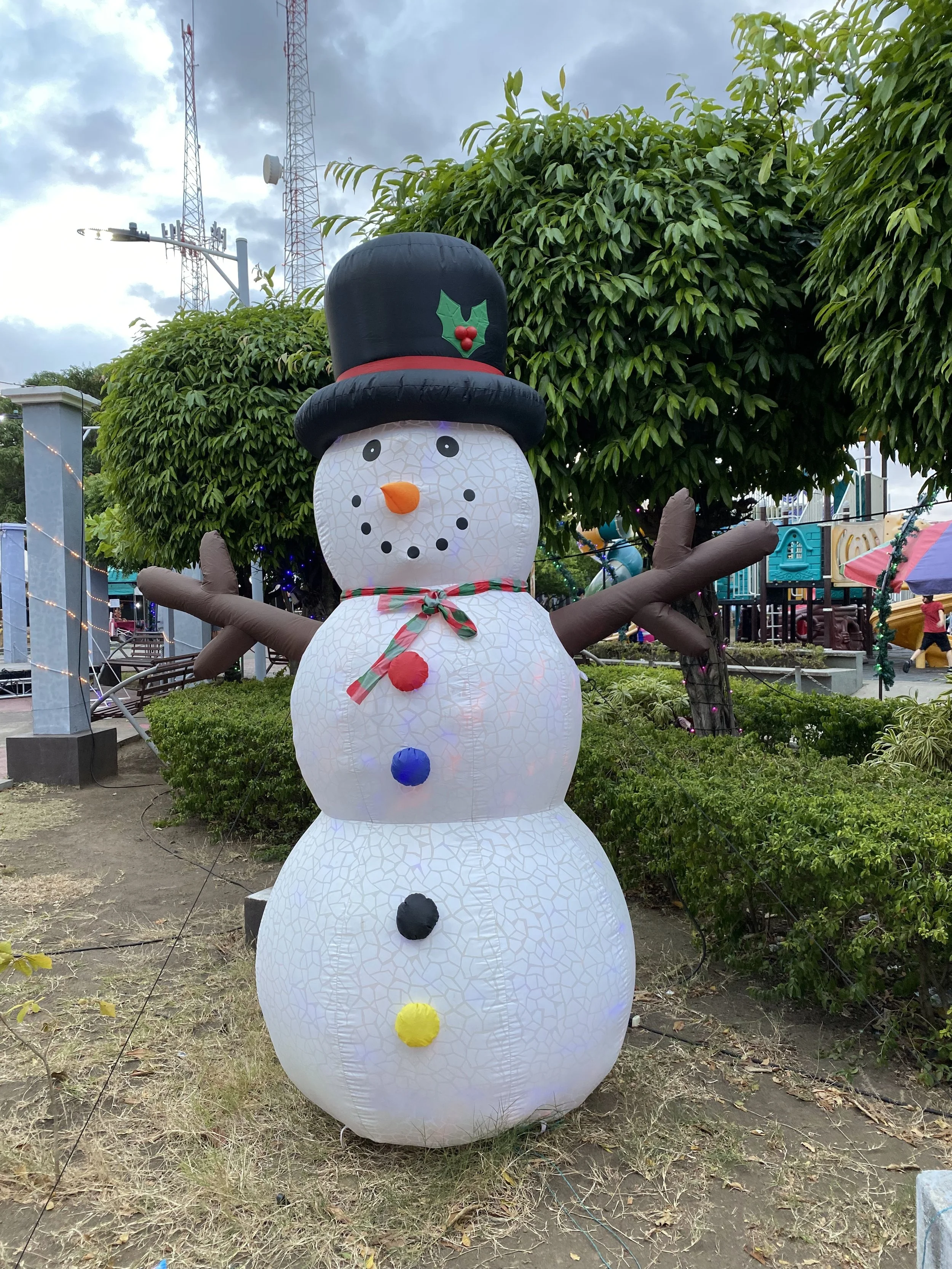 Inflatable Christmas snowman decoration in a tropical park in Rivas, Nicaragua, surrounded by green trees and warm evening weather.