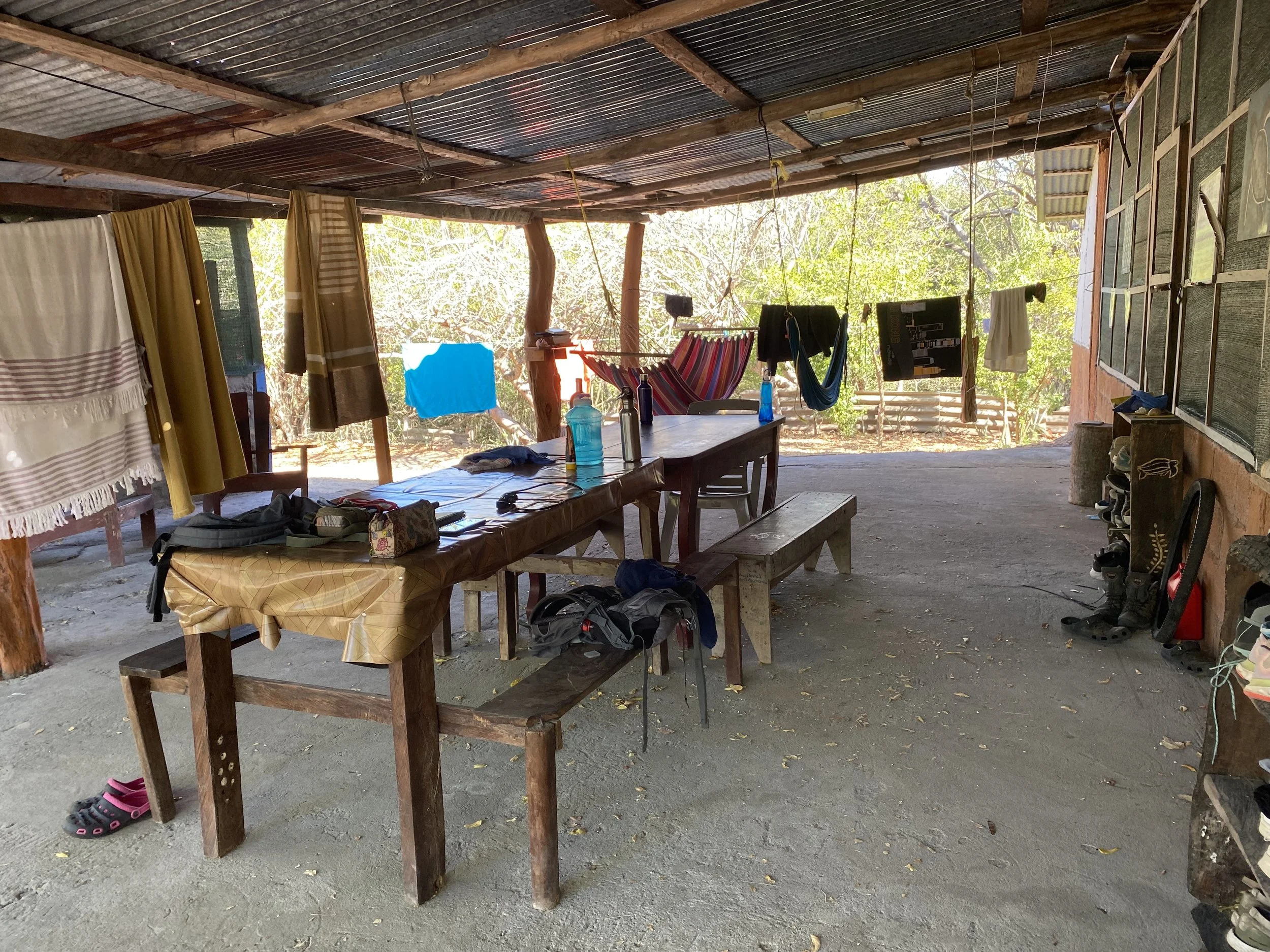 Open-air common area at the Cabuyal sea turtle conservation camp in Costa Rica, with wooden tables, benches, hammocks, towels and clothing hanging to dry.