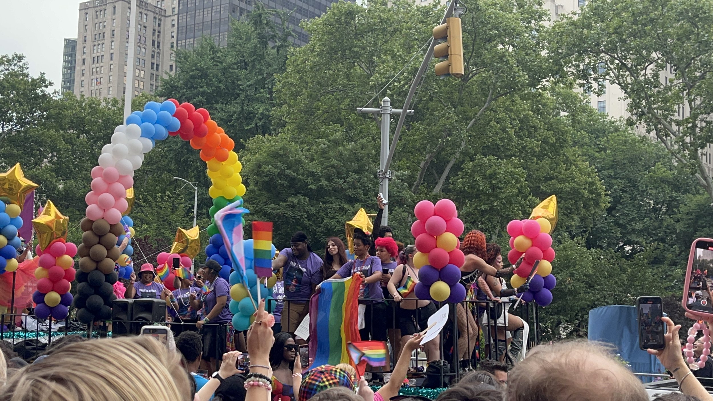 A colourful Pride parade float surrounded by large crowds in New York City.
