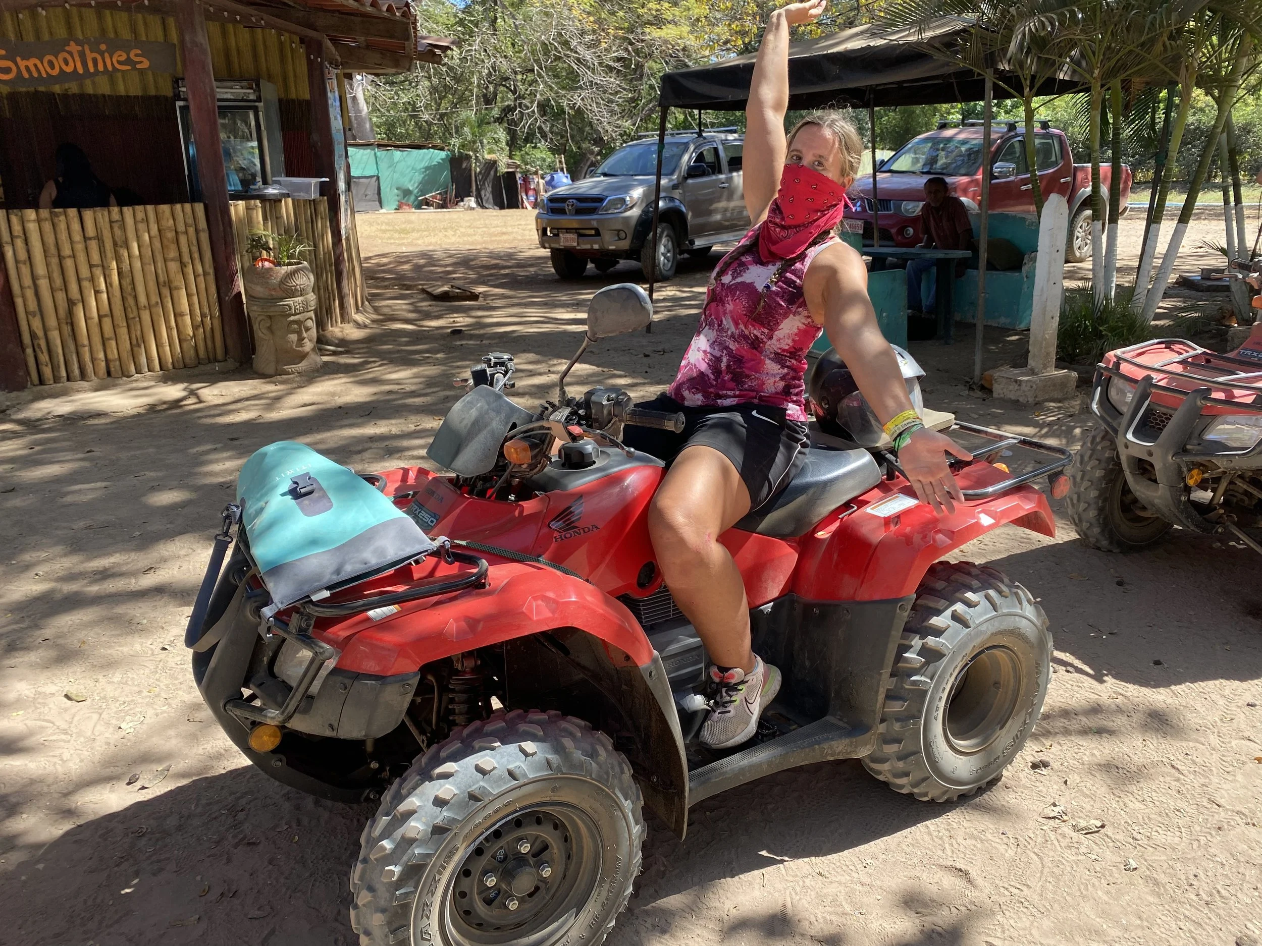 A traveller wearing a helmet and red bandana sits on a red ATV in Tamarindo, Costa Rica, posing excitedly before beginning an off-road tour through the Guanacaste countryside.