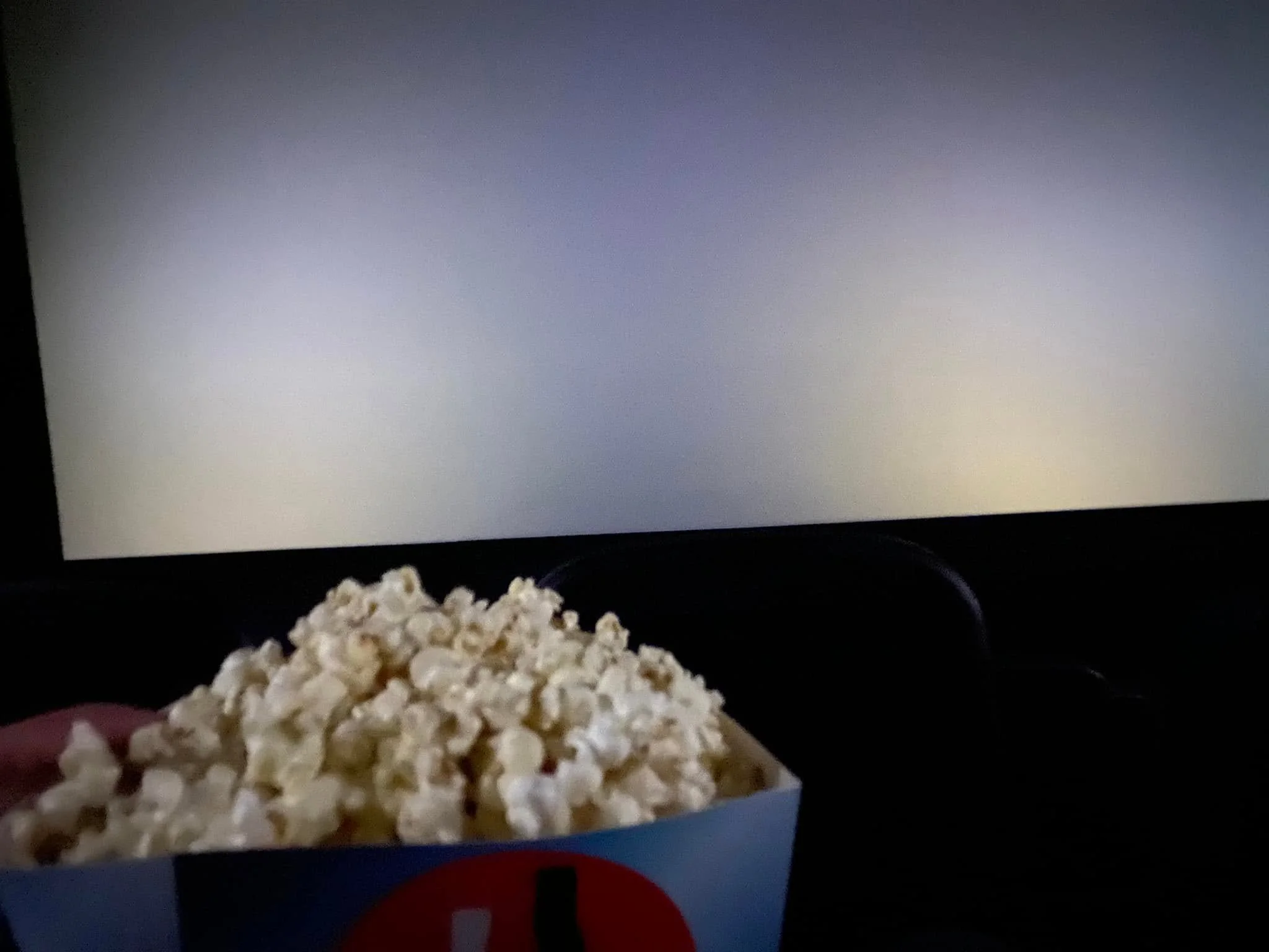 Box of popcorn held in front of a cinema screen during a movie in San José, Costa Rica.