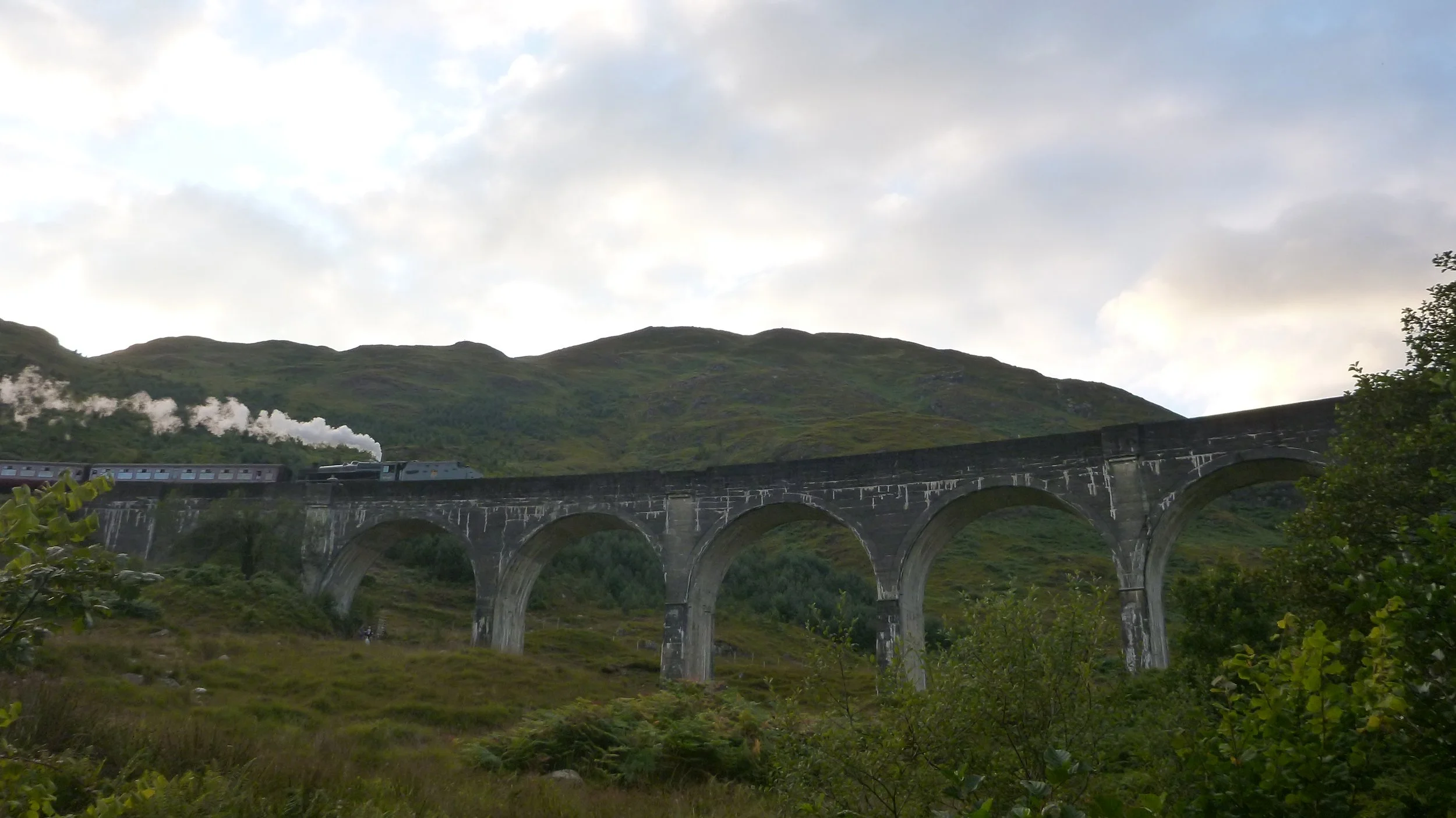 steam train crossing glenfinnan viaduct in scotland