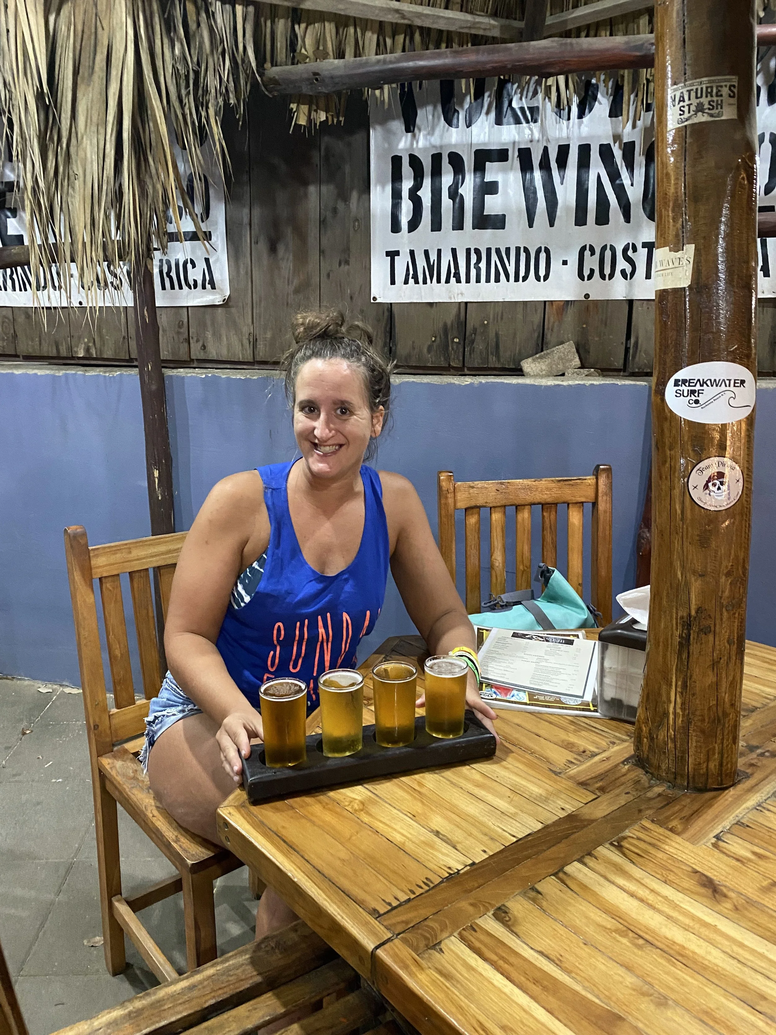A woman sitting at a brewery in Tamarindo, Costa Rica, with a flight of four local craft beers on a wooden table.