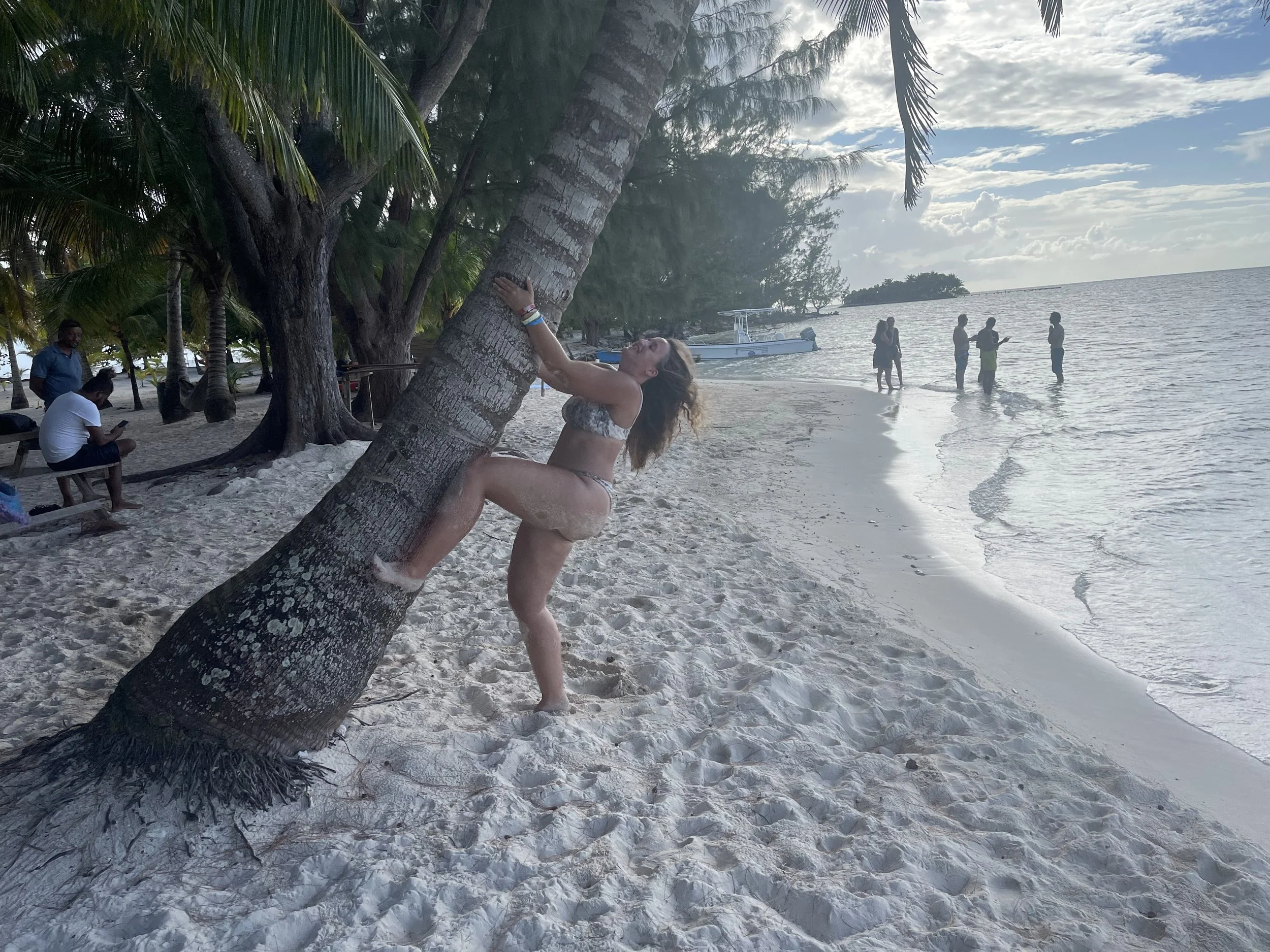Woman in a bikini attempting to pose on a leaning palm tree on a sandy beach at White Island near Utila.