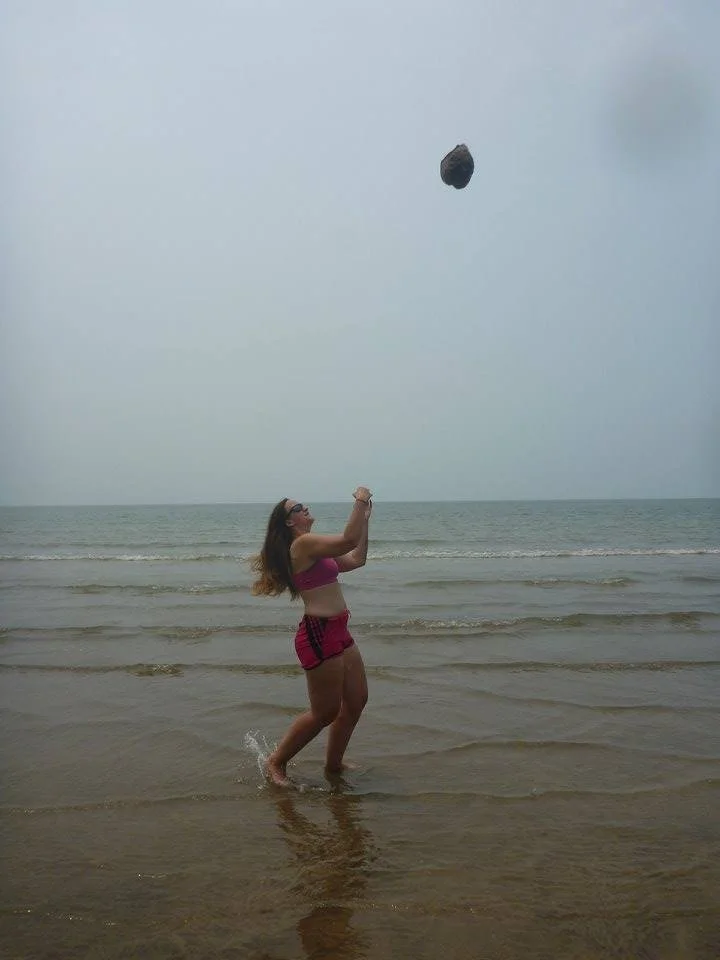Woman trying to catch a coconut on beach during solo travel representing chasing experiences while traveling