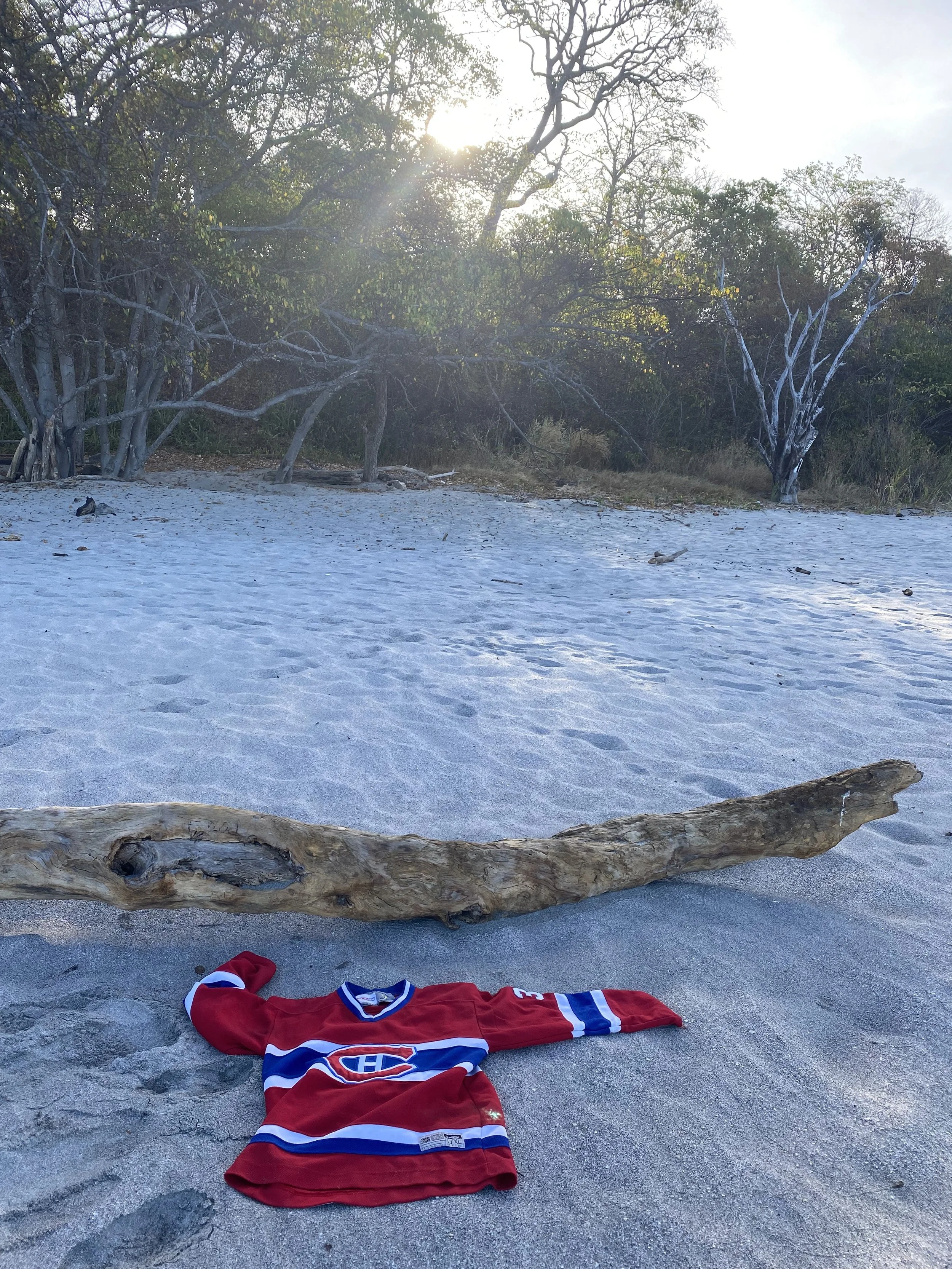 Red Montreal Canadiens hockey jersey laid on the sand beside driftwood at Playa Cabuyal in Costa Rica.