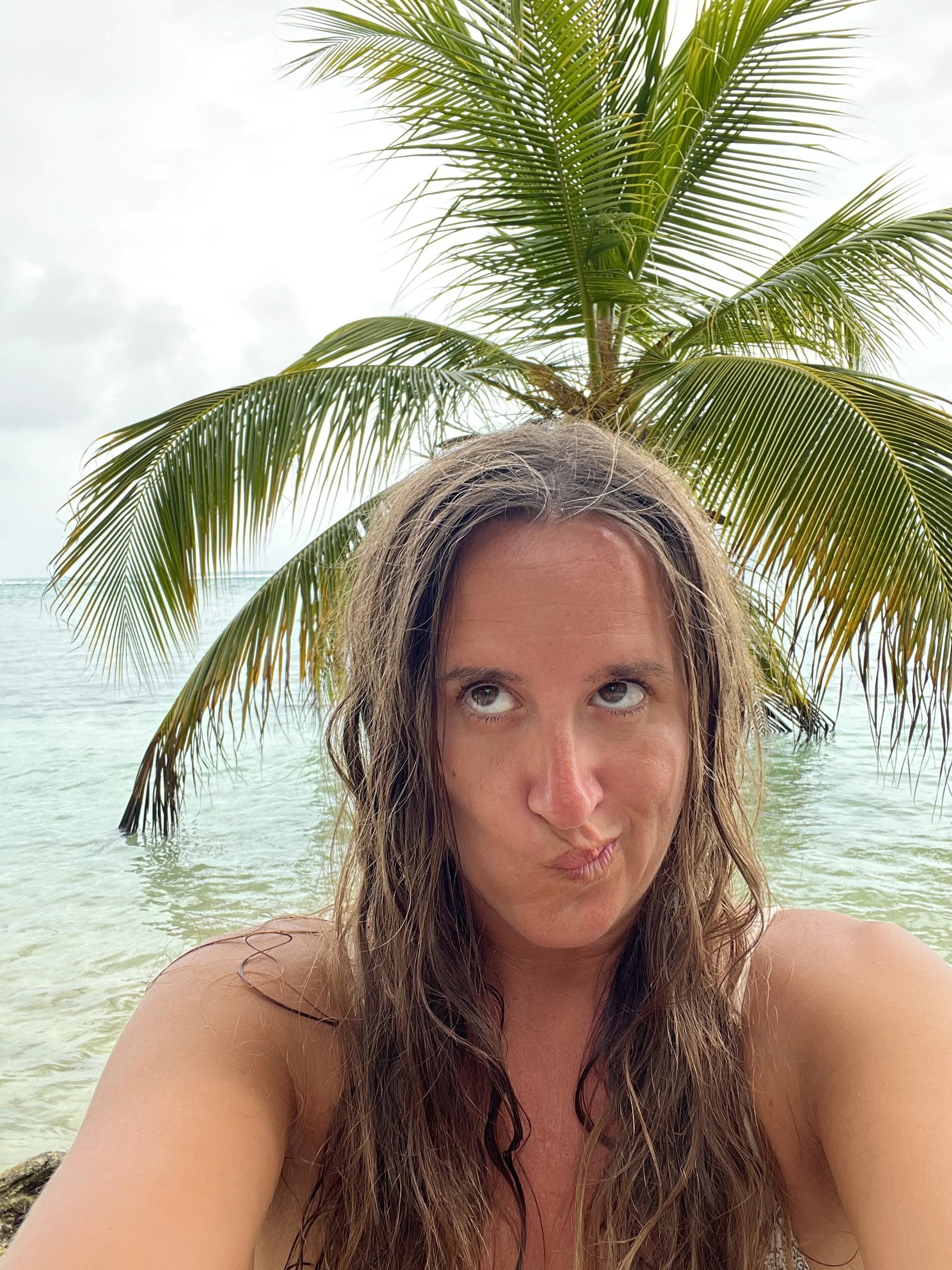 Woman taking a playful selfie in front of a palm tree and clear tropical water on one of Panama’s San Blas Islands.