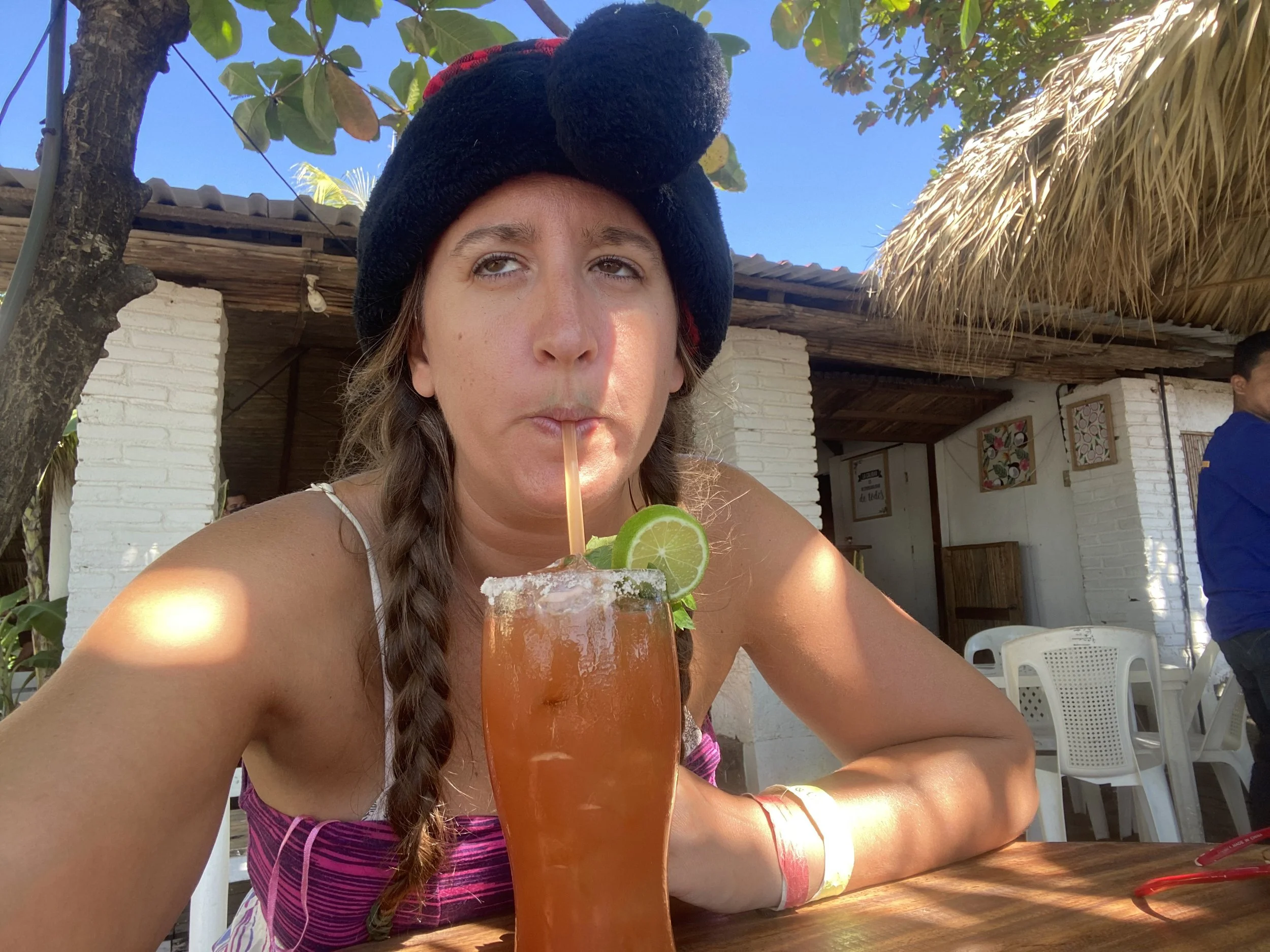 Woman in a winter hat drinking a cocktail at an outdoor beachside restaurant in Las Peñitas during Christmas.