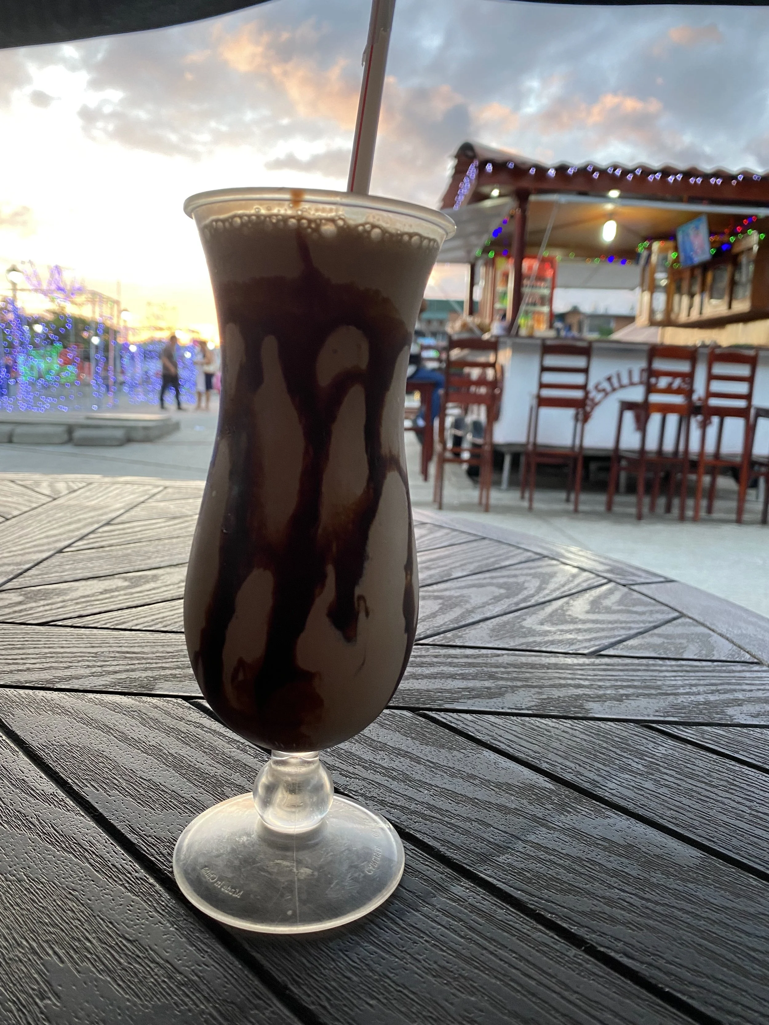 Chocolate milkshake on an outdoor table in Rivas, Nicaragua with the town square and evening lights in the background.