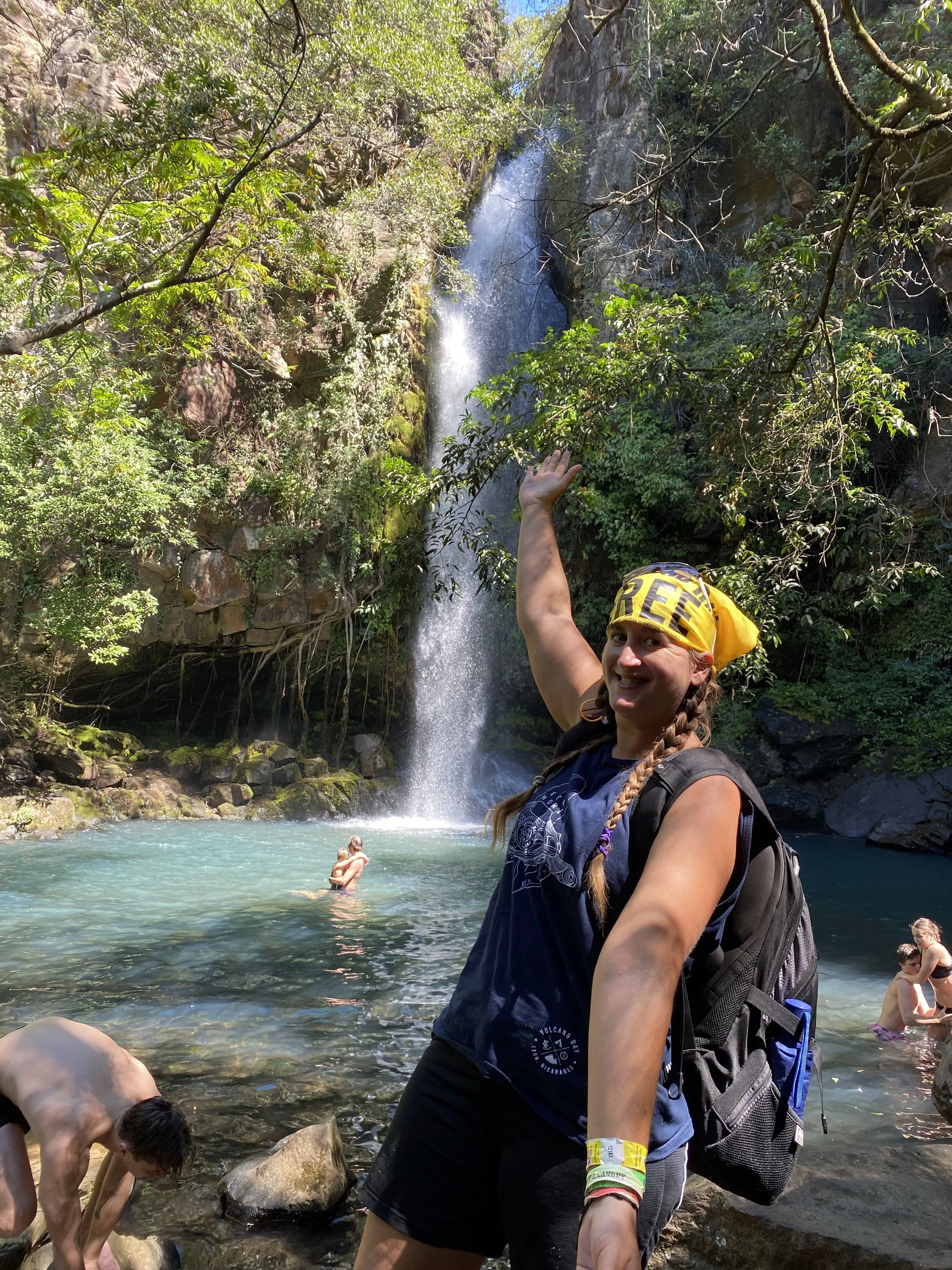 Backpacker standing in front of a waterfall at Rincón de la Vieja National Park in Costa Rica, with a turquoise pool and lush forest in the background.