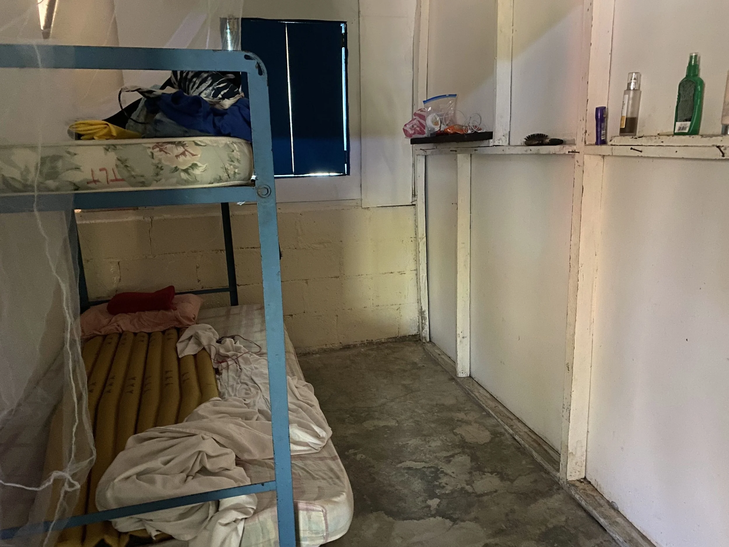 Simple volunteer bedroom at the Cabuyal sea turtle conservation camp in Costa Rica, with metal bunk beds, mosquito netting, shelves and a concrete floor.