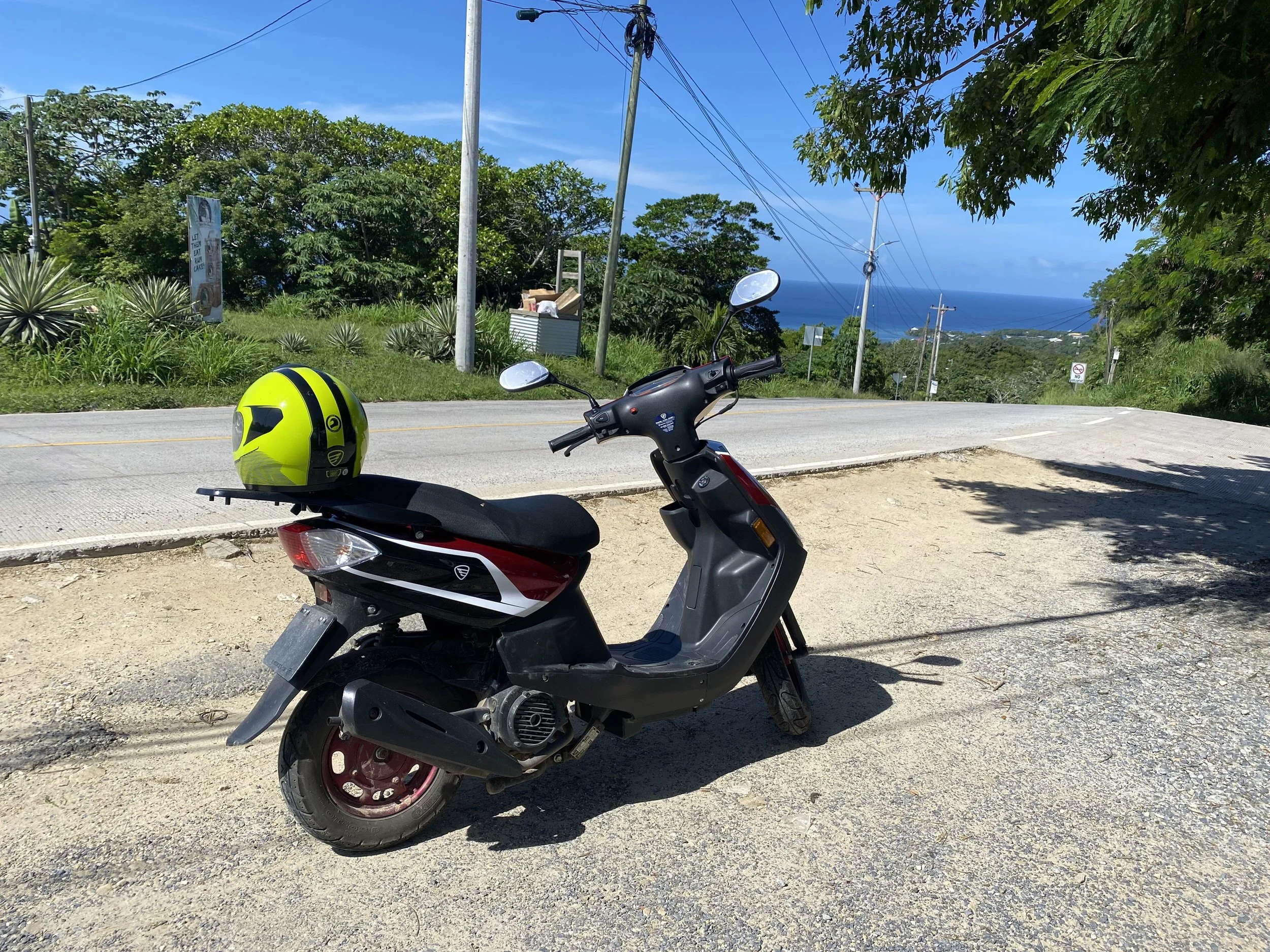 Motorbike parked at a scenic roadside viewpoint in Roatán, Honduras with ocean views and greenery